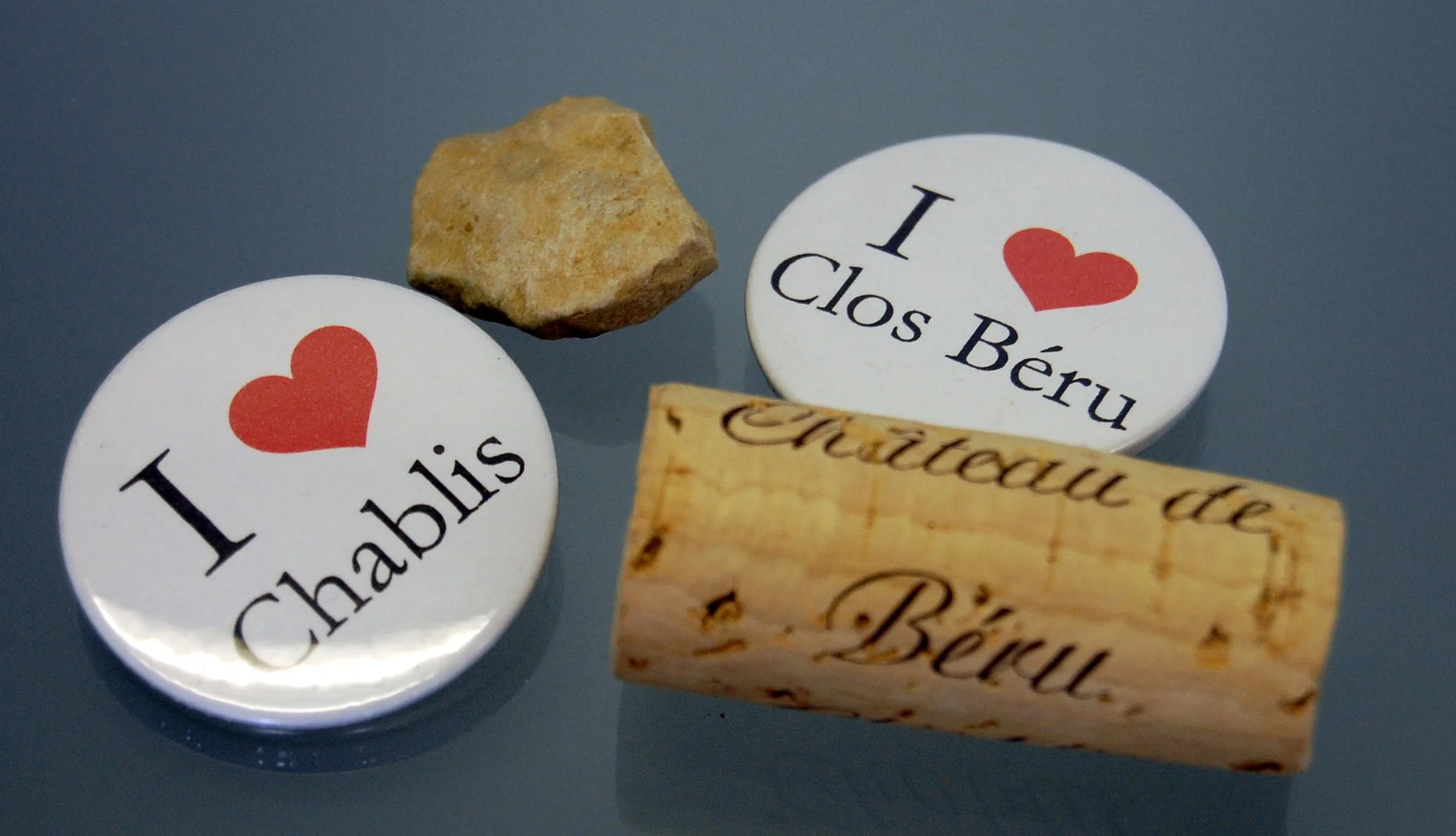Chablis wine memorabilia featuring Clos Béru cork, collectible pins, and limestone rock representing the Burgundy wine region and Chablis wine culture.