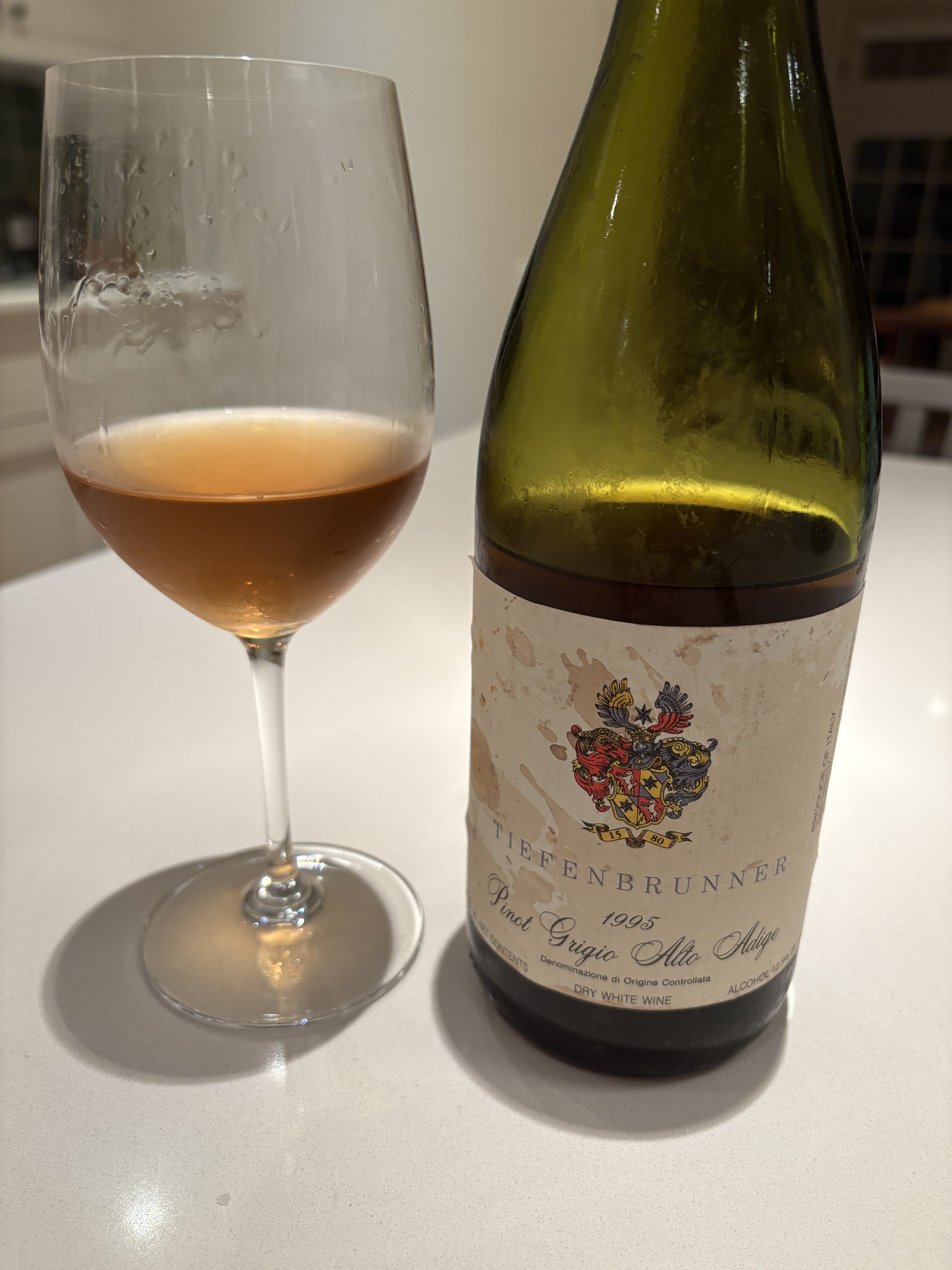 Glass of aged white wine with darker color next to bottle, showing signs of oxidation and aging