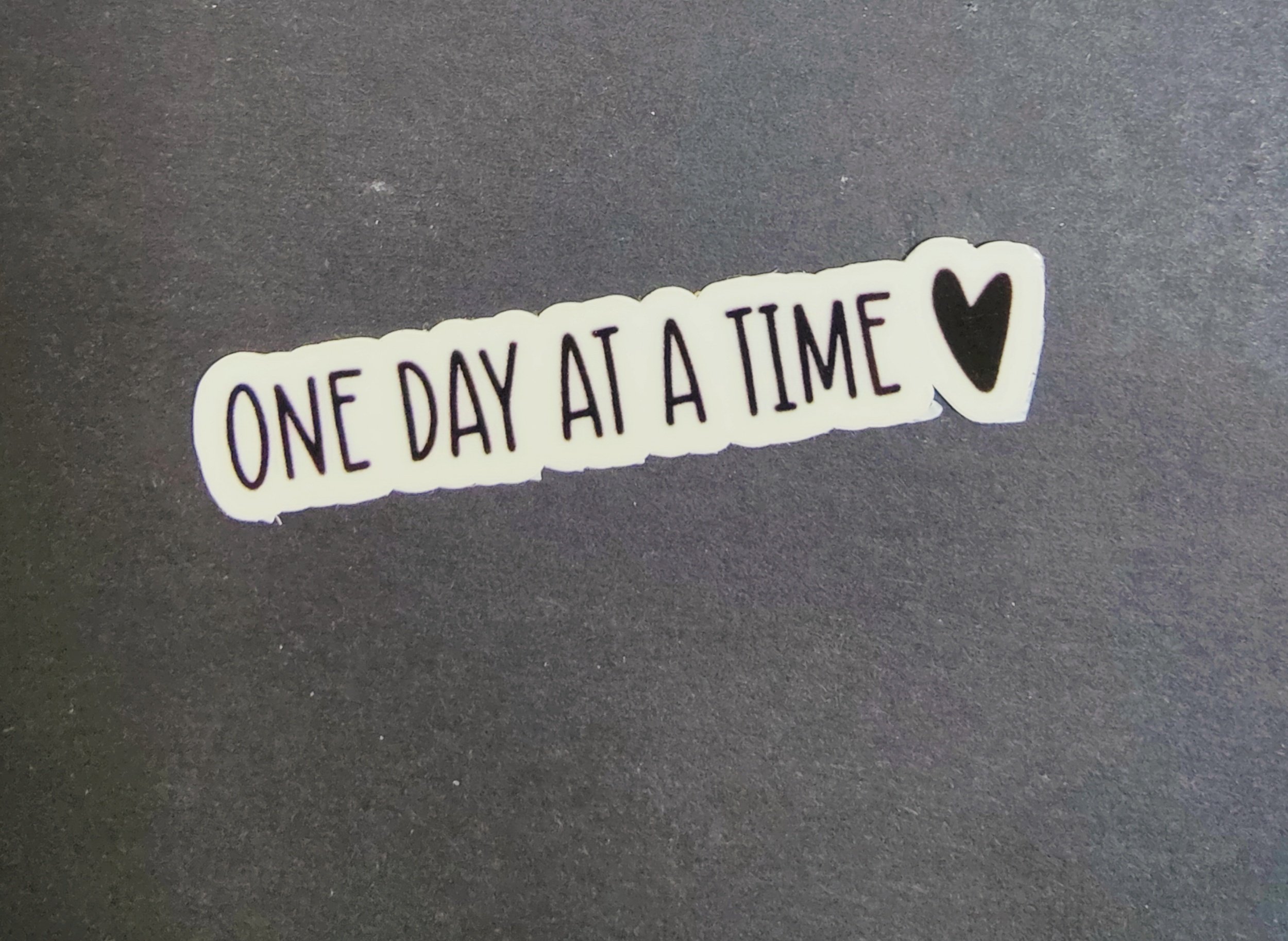 Sticker with "One Day At A Time" and a small heart