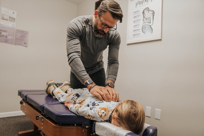 Chiropractor Dr. Jeremy Lawson adjusting a child on a table in a clinic.