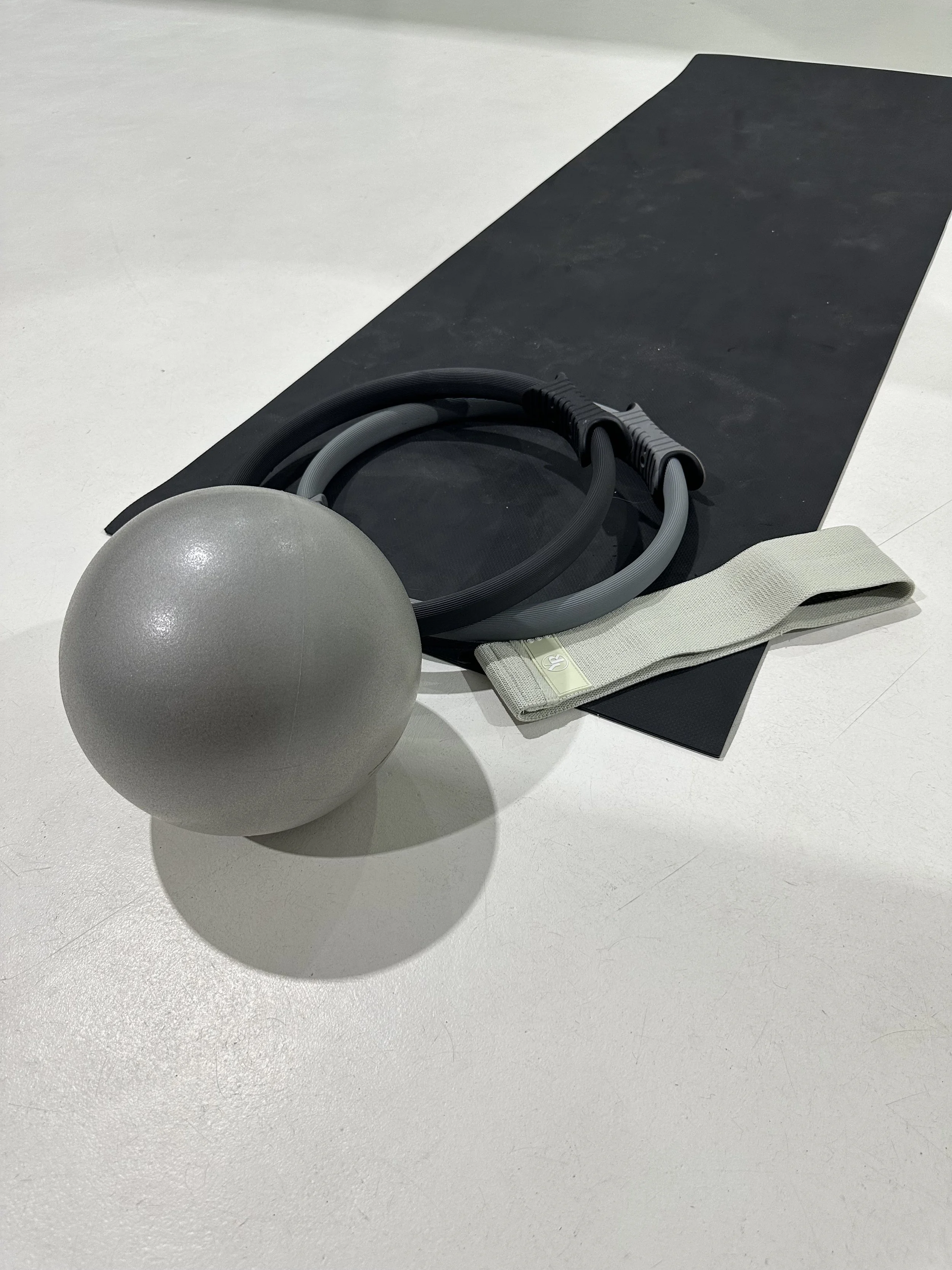 Exercise mat, resistance bands, wall ball, and yoga strap on a white floor.
