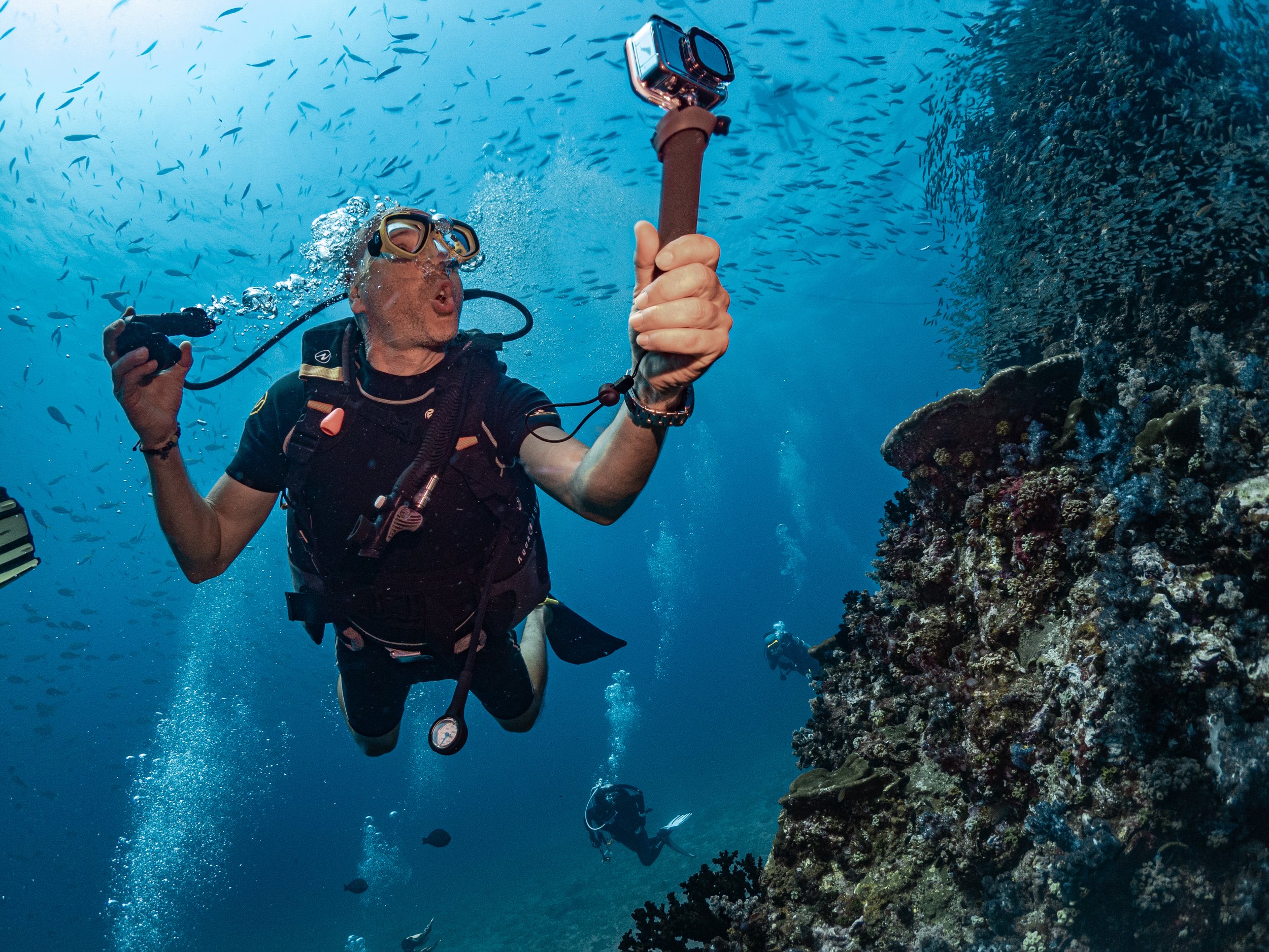 Subacqueo che registra un video con una action cam mentre nuota vicino a una barriera corallina.