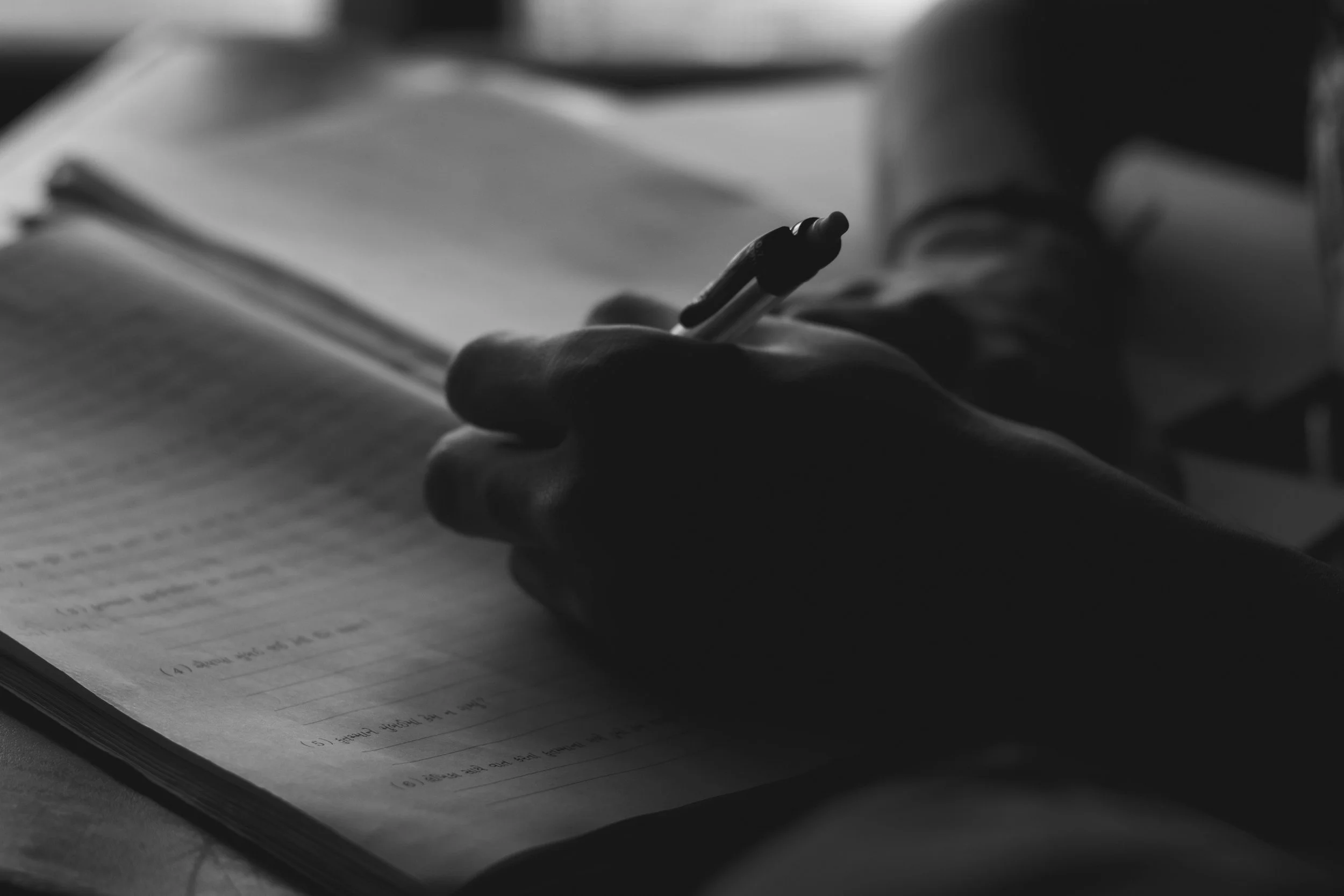 A hand holding a pen and writing in a notebook, black and white photo.