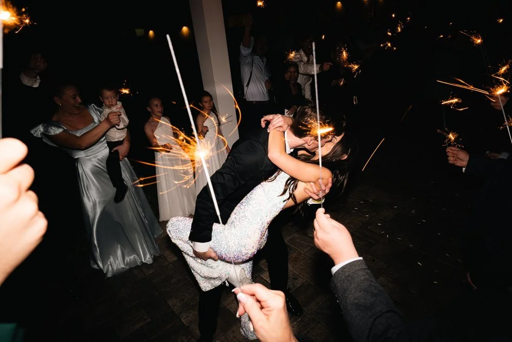 Bride and groom kissing surrounded by people holding sparklers at night.