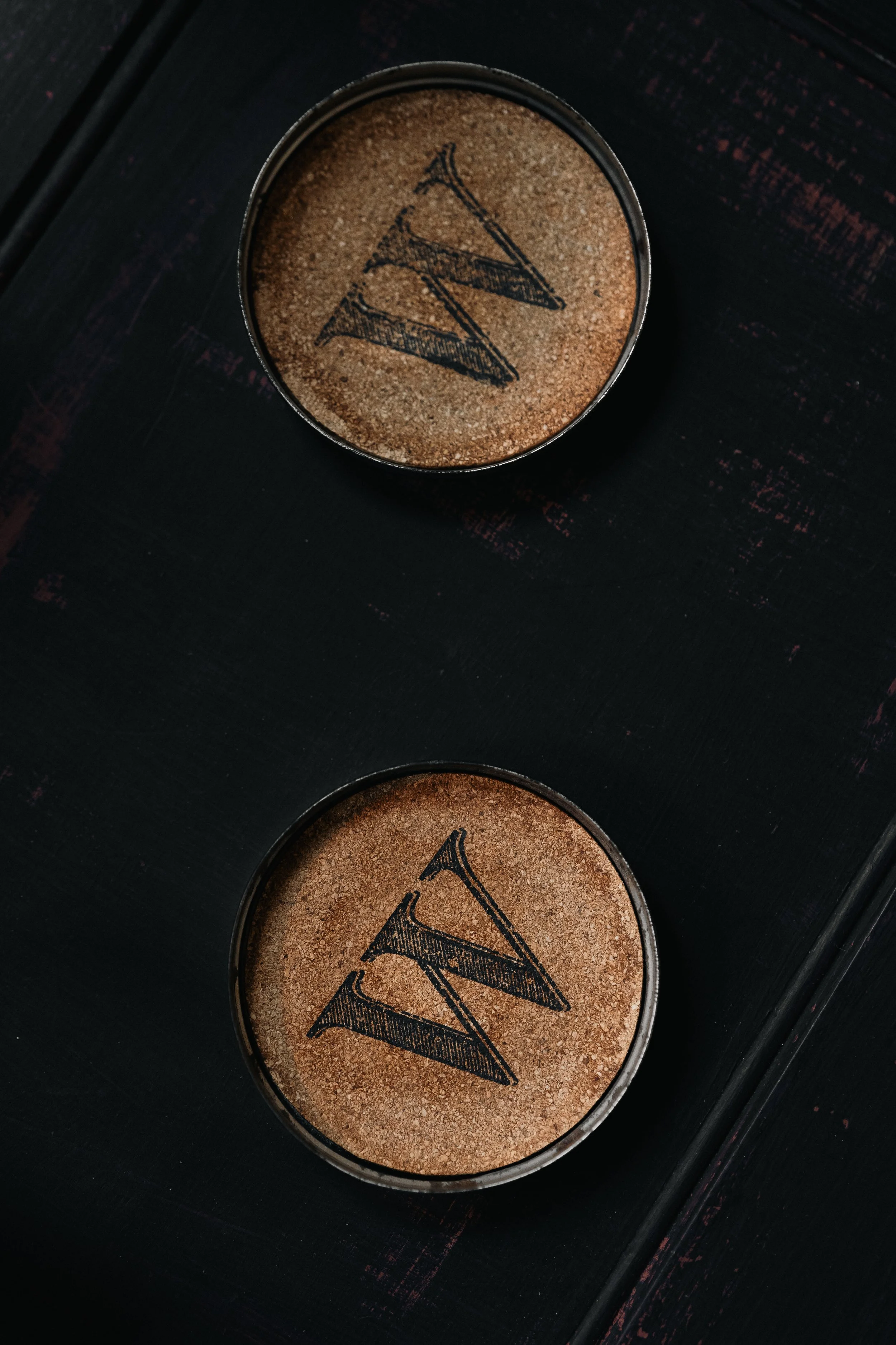 Two brown coasters with the letter 'W' on a dark background.