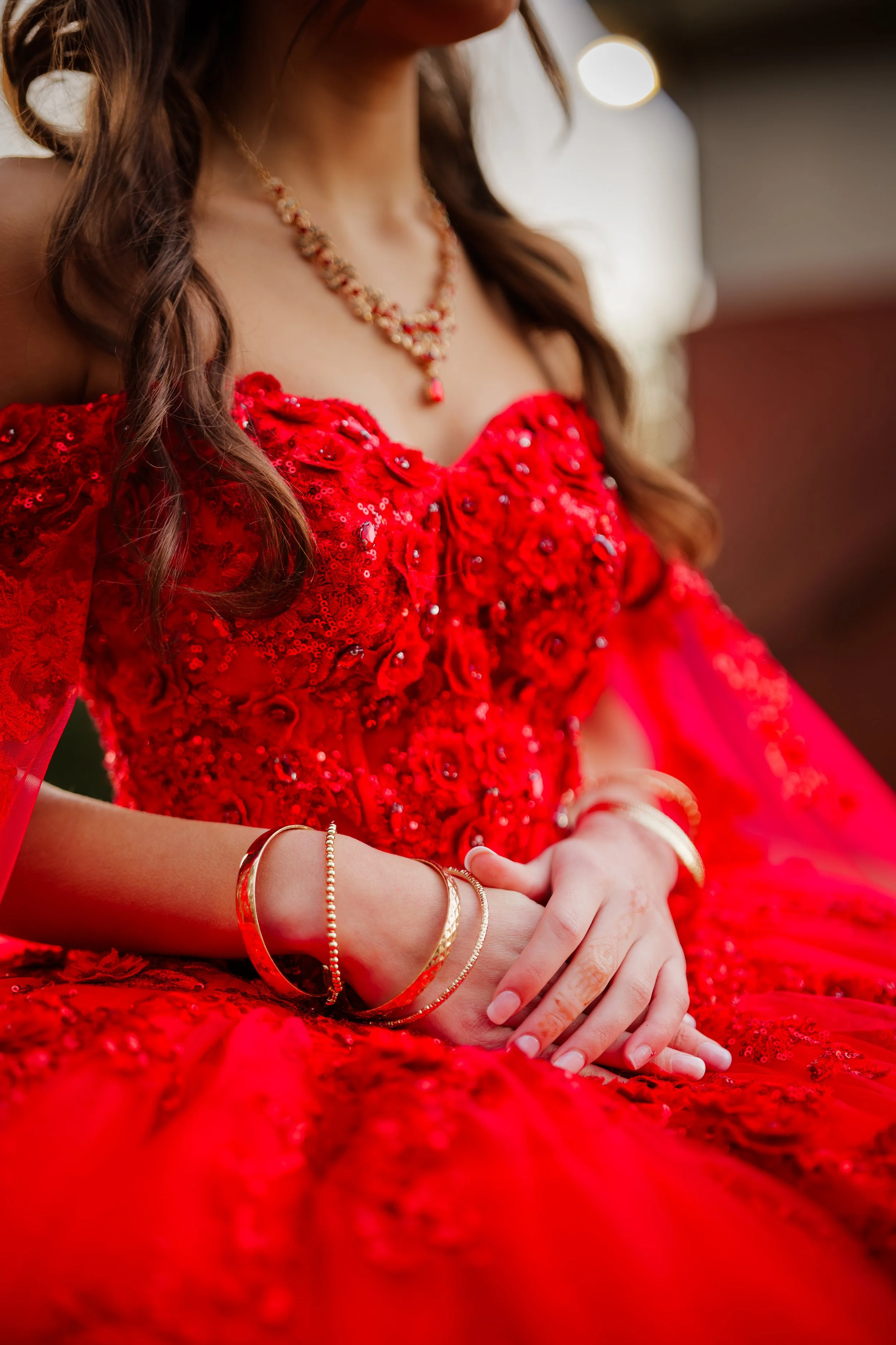 Woman wearing an ornate red dress with gold bracelets and necklace, hands clasped.
