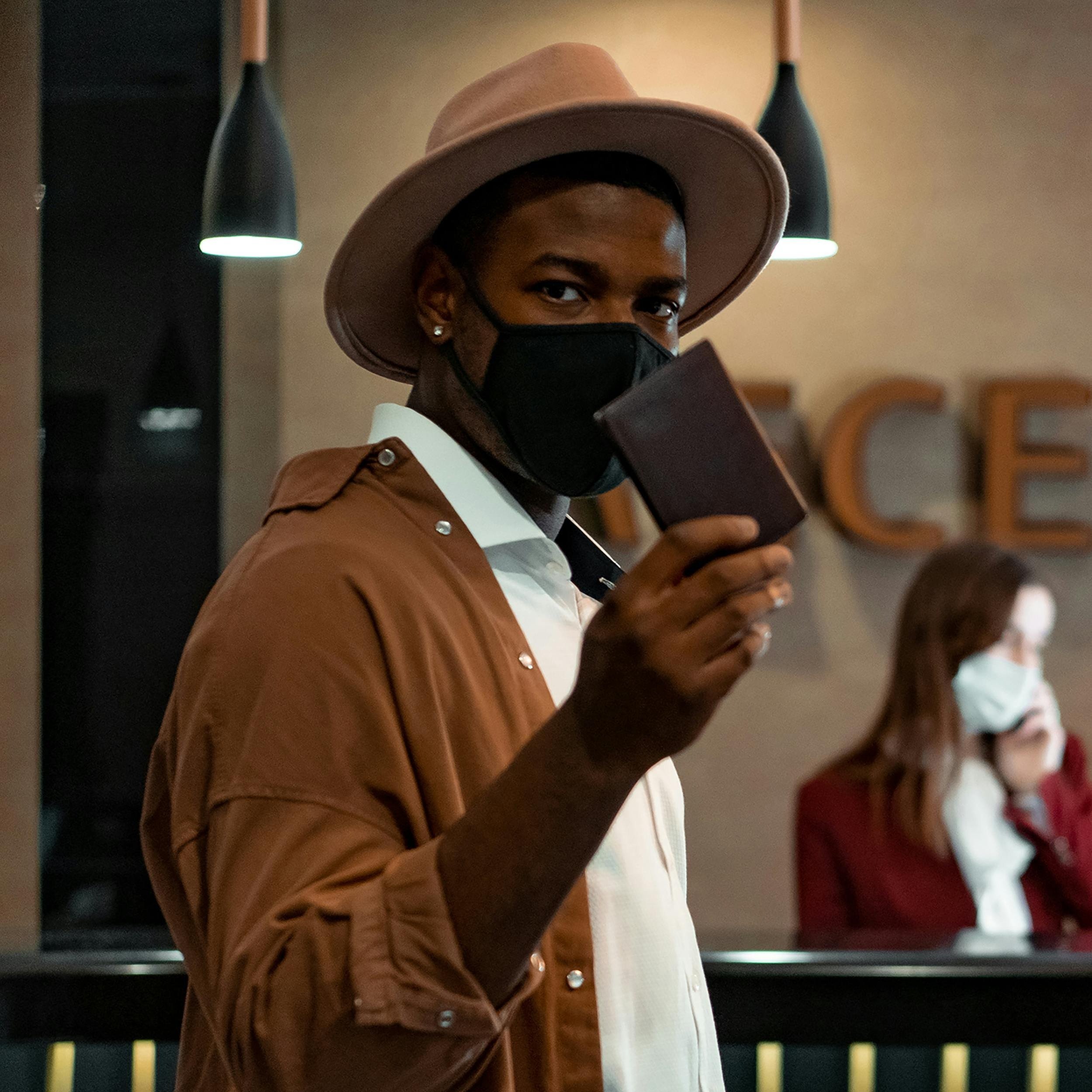 Man in hat showing passport at hotel reception, wearing a mask.