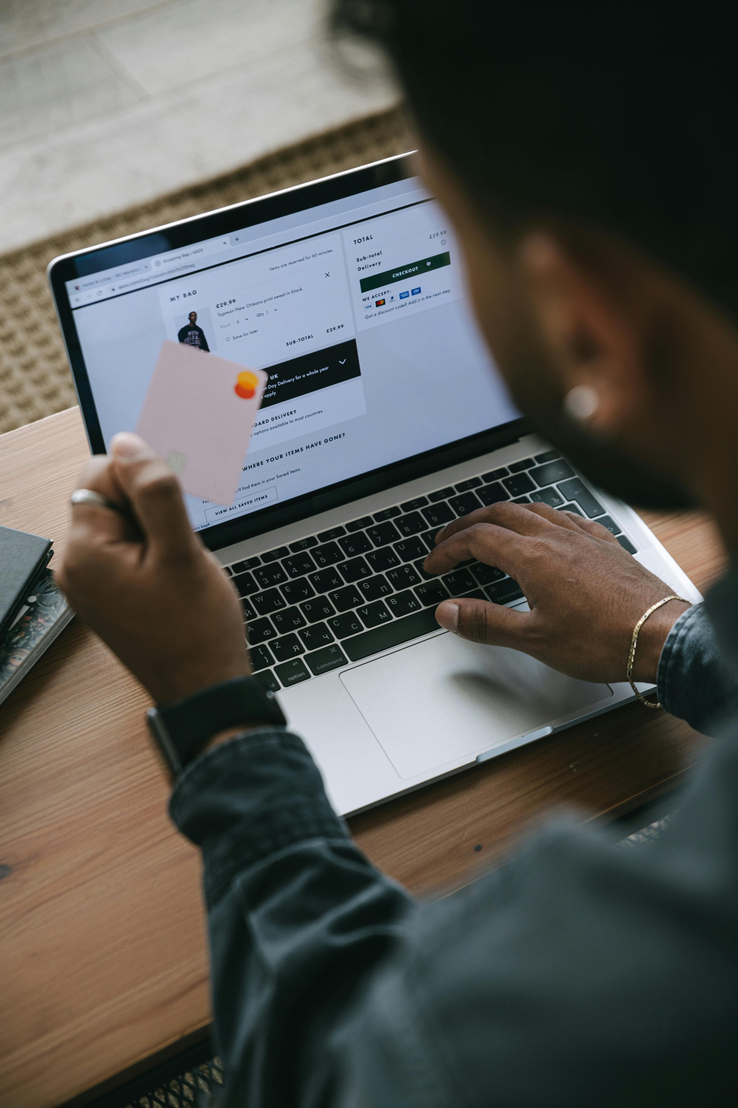 Person holding a credit card while using a laptop for online shopping at a desk.