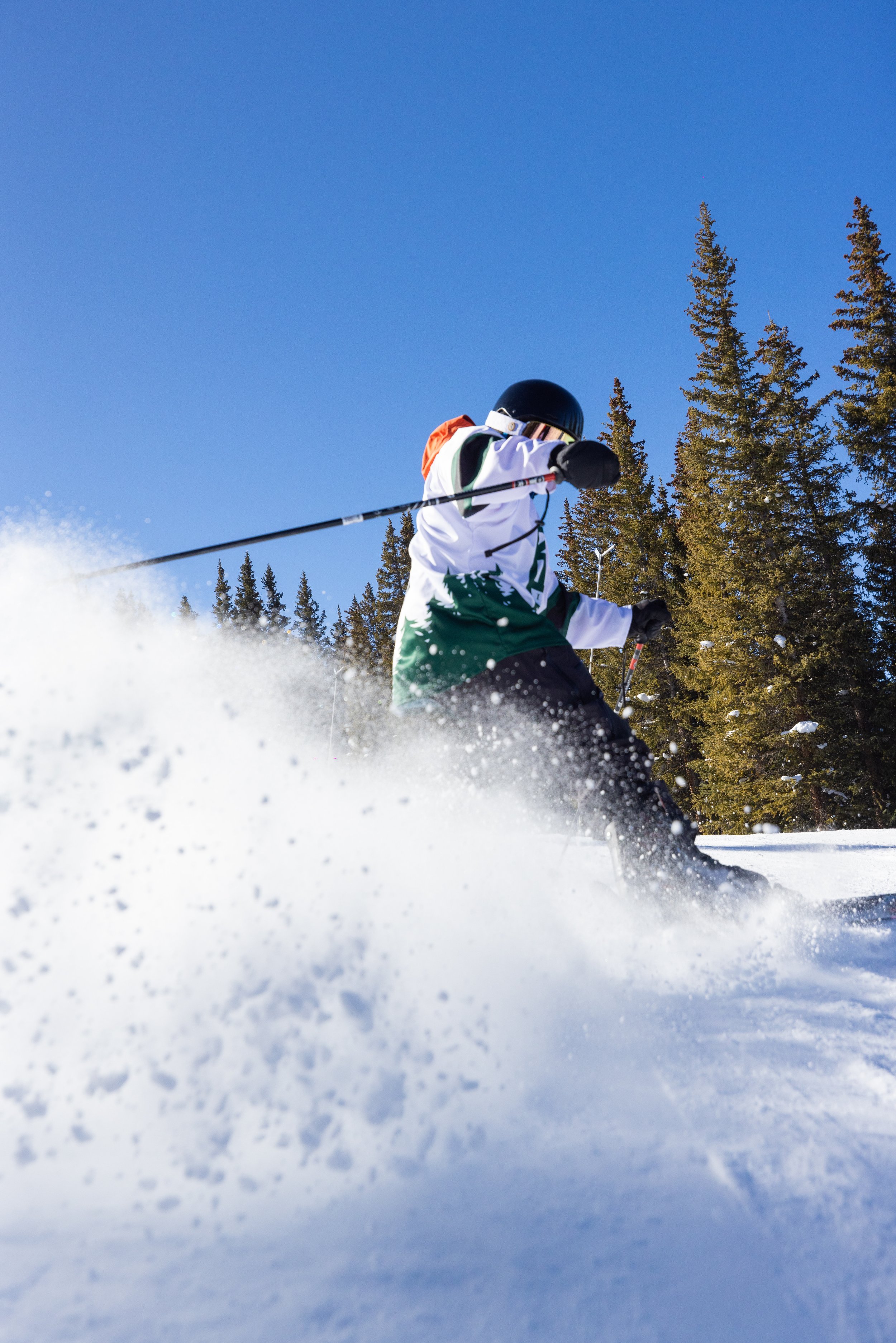 Group of snowboarders and skiers in line at a snowy ski resort with background of buildings and mountains.