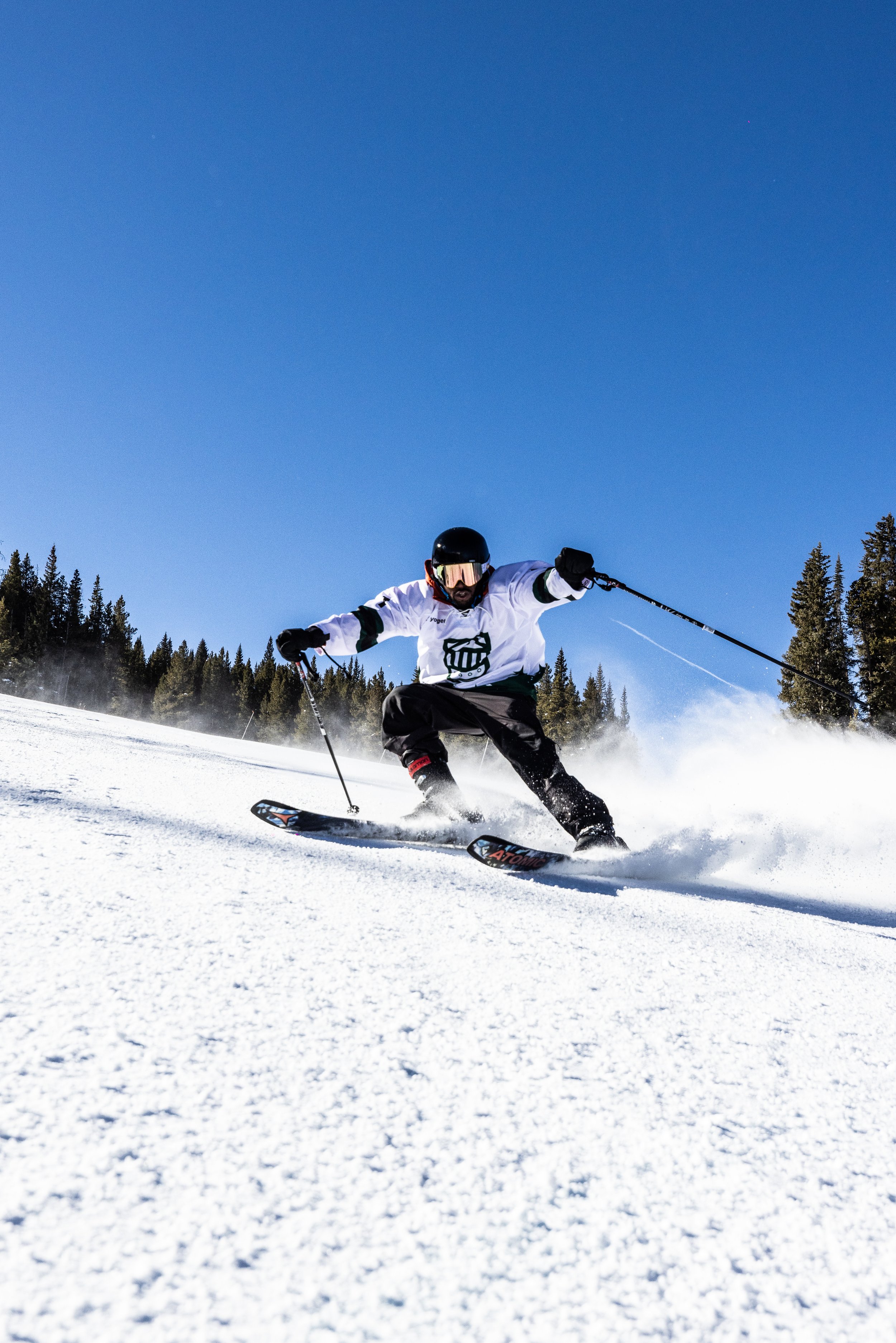 A snowboarder wearing a goggles skiing downhill on a snowy slope on a clear blue day.