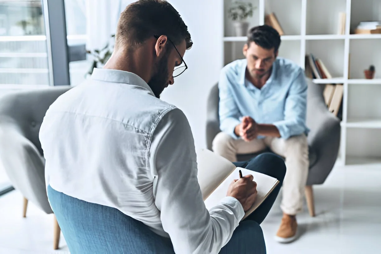 Therapist taking notes during a counseling session with a client in an office setting.