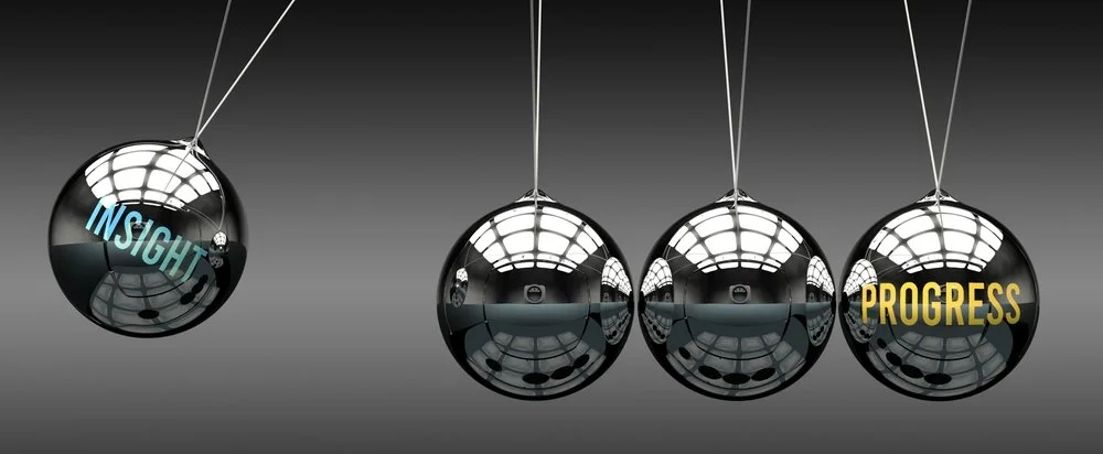 Four black spheres hanging from strings with the words "Insight" and "Progress" on two of them, reflecting a ceiling with bright lights.
