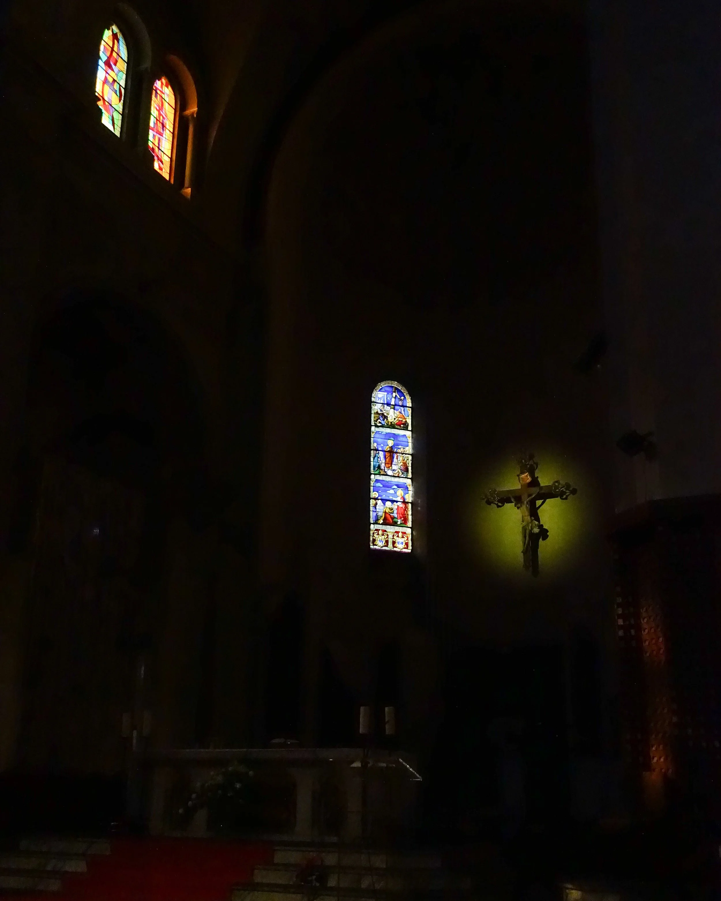 Vitraux colorés et crucifix dans une église sombre.