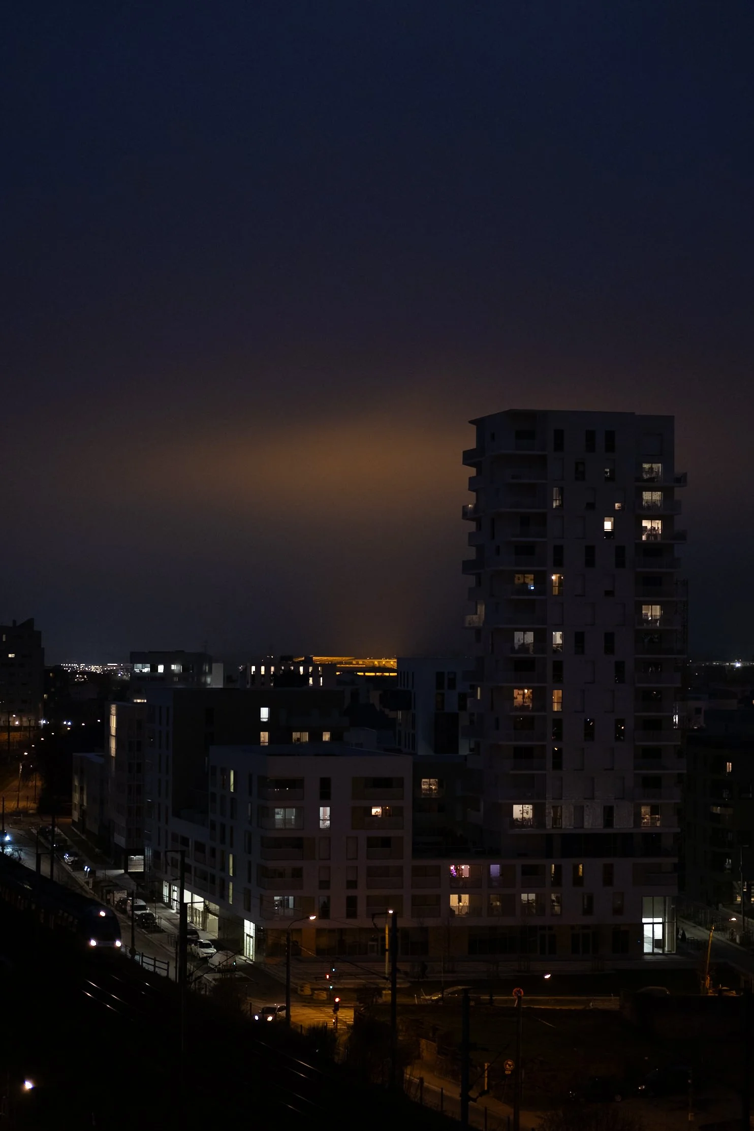 Vue nocturne de plusieurs immeubles résidentiels avec quelques fenêtres éclairées et un ciel sombre avec une lumière diffuse à l'horizon.