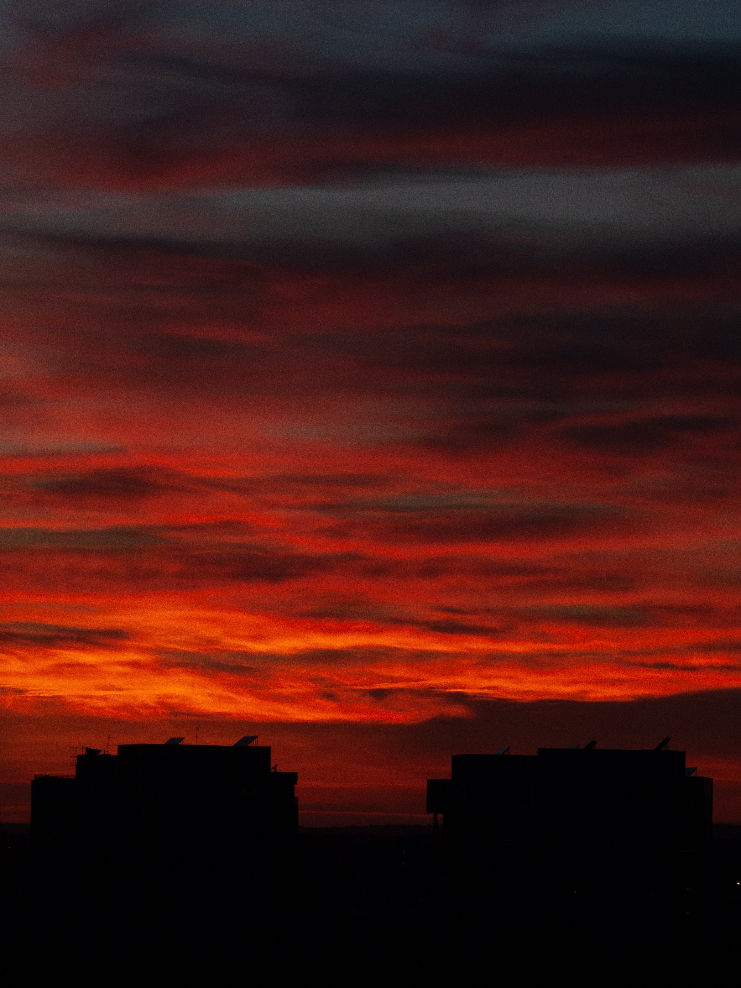 Coucher de soleil avec un ciel coloré en rouge et noir, silhouette de bâtiments en bas.