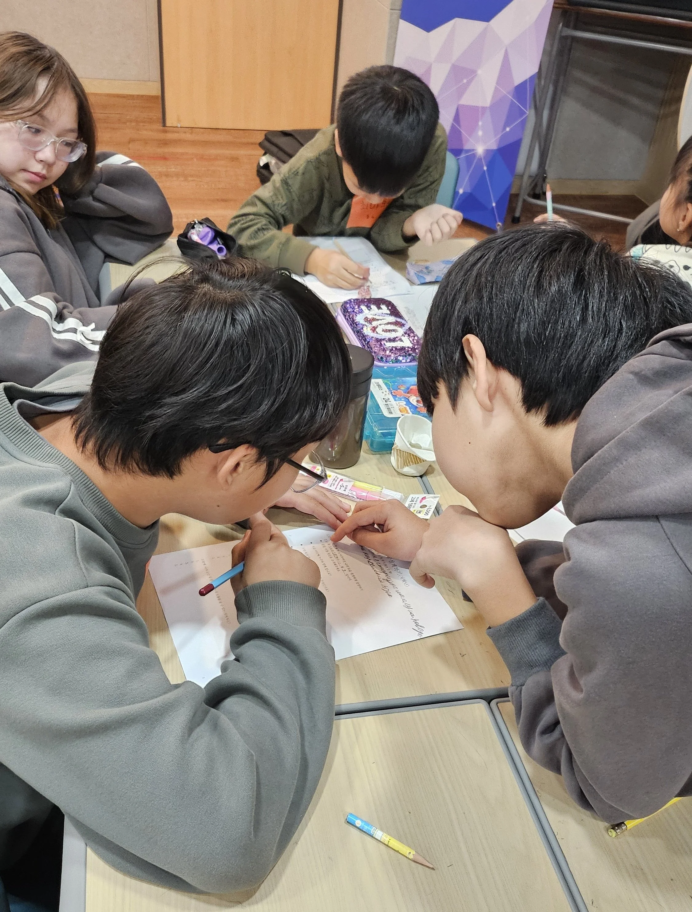 Children gathered around a table working together on a paper in a classroom setting.