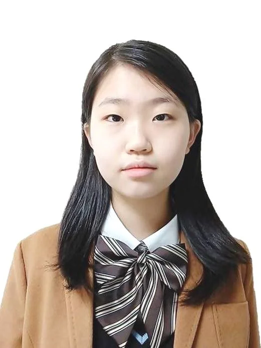 A young Asian girl with long black hair, wearing a school uniform with a white shirt, a dark tie with stripes, and a brown blazer, posing against a plain white background.