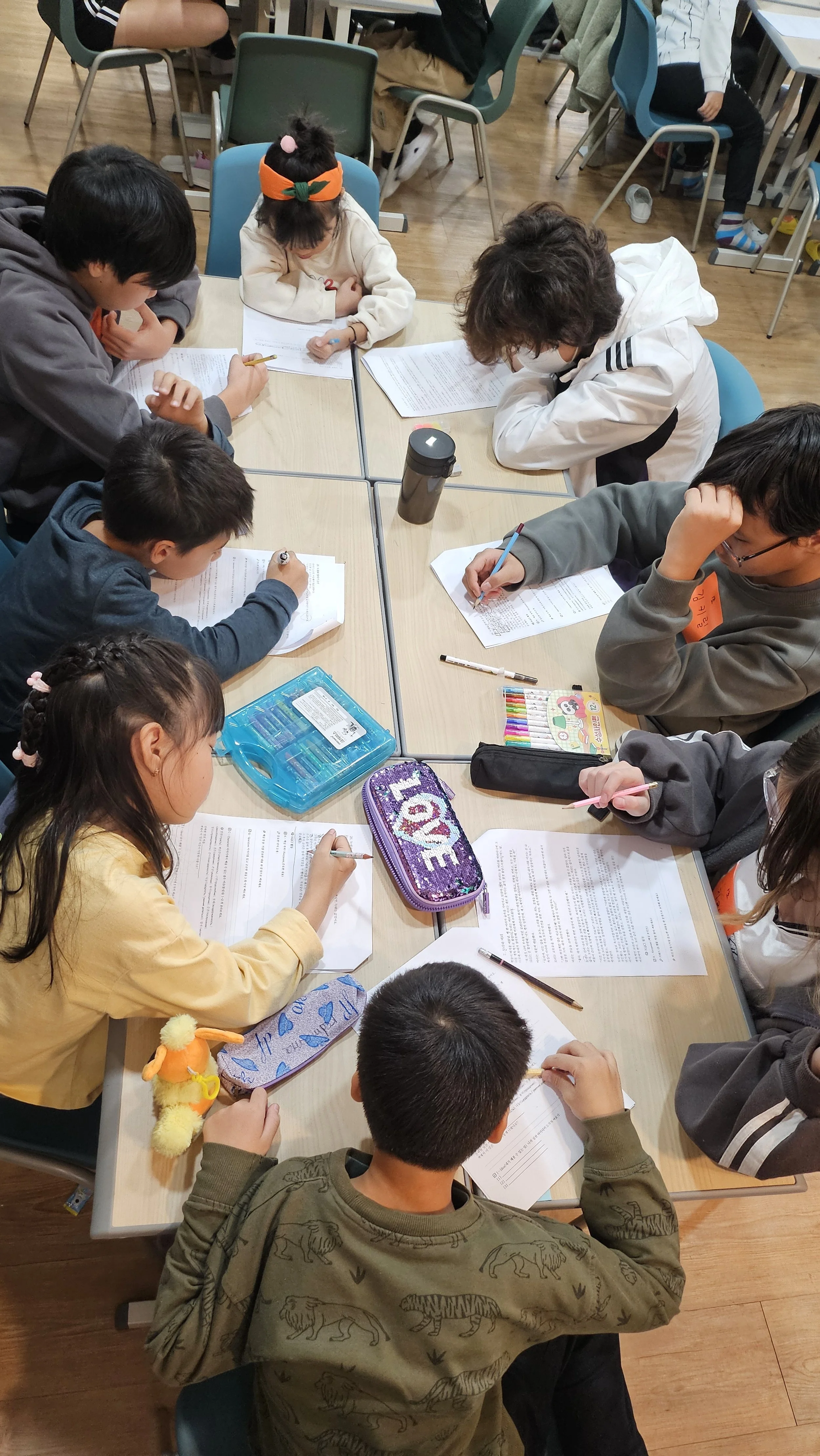 Children studying and doing homework at a classroom table with notebooks, pens, and school supplies.