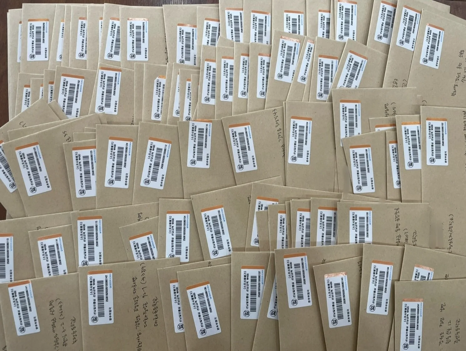Numerous manila envelopes with white barcode labels arranged on a wooden surface.