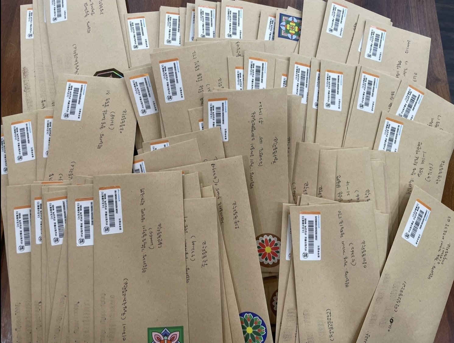 Multiple brown envelopes with barcodes and handwritten addresses spread out on a wooden surface.