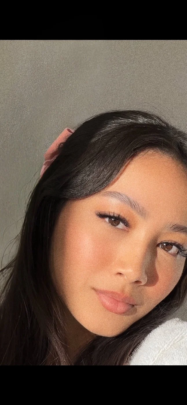 Femme avec cheveux longs foncés, regardant vers l'objectif, portant un accessoire rose dans les cheveux.