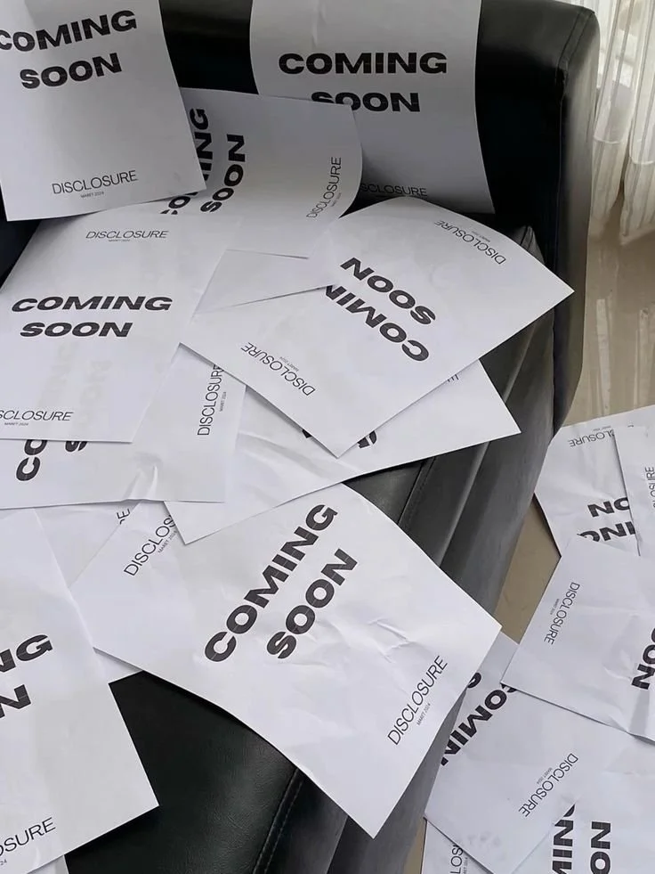 Feuilles de papier avec l'inscription "Coming Soon" dispersées sur un canapé noir.