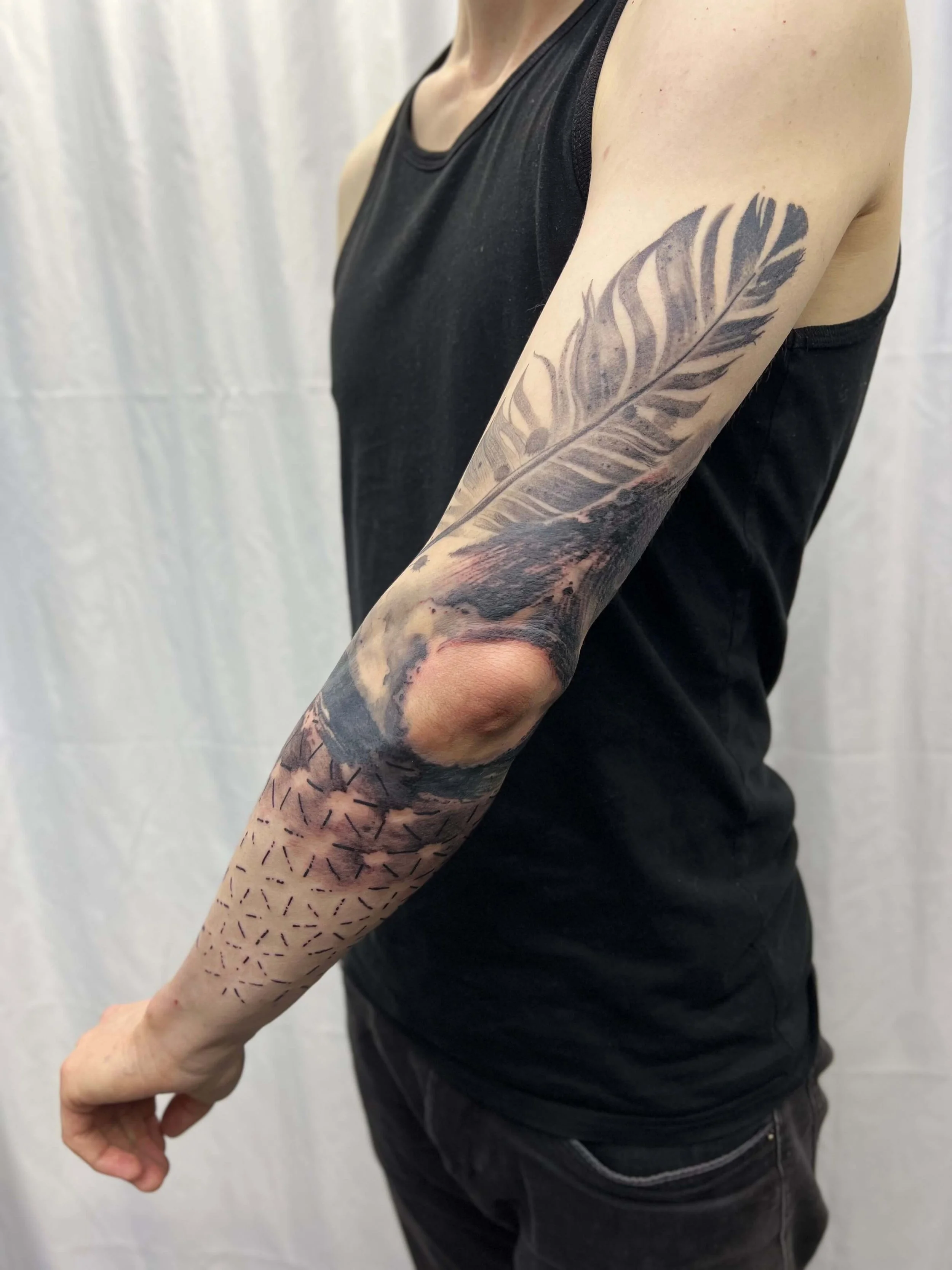 Black and grey feather tattoo combined with geometric pattern work and abstract landscape detailing.