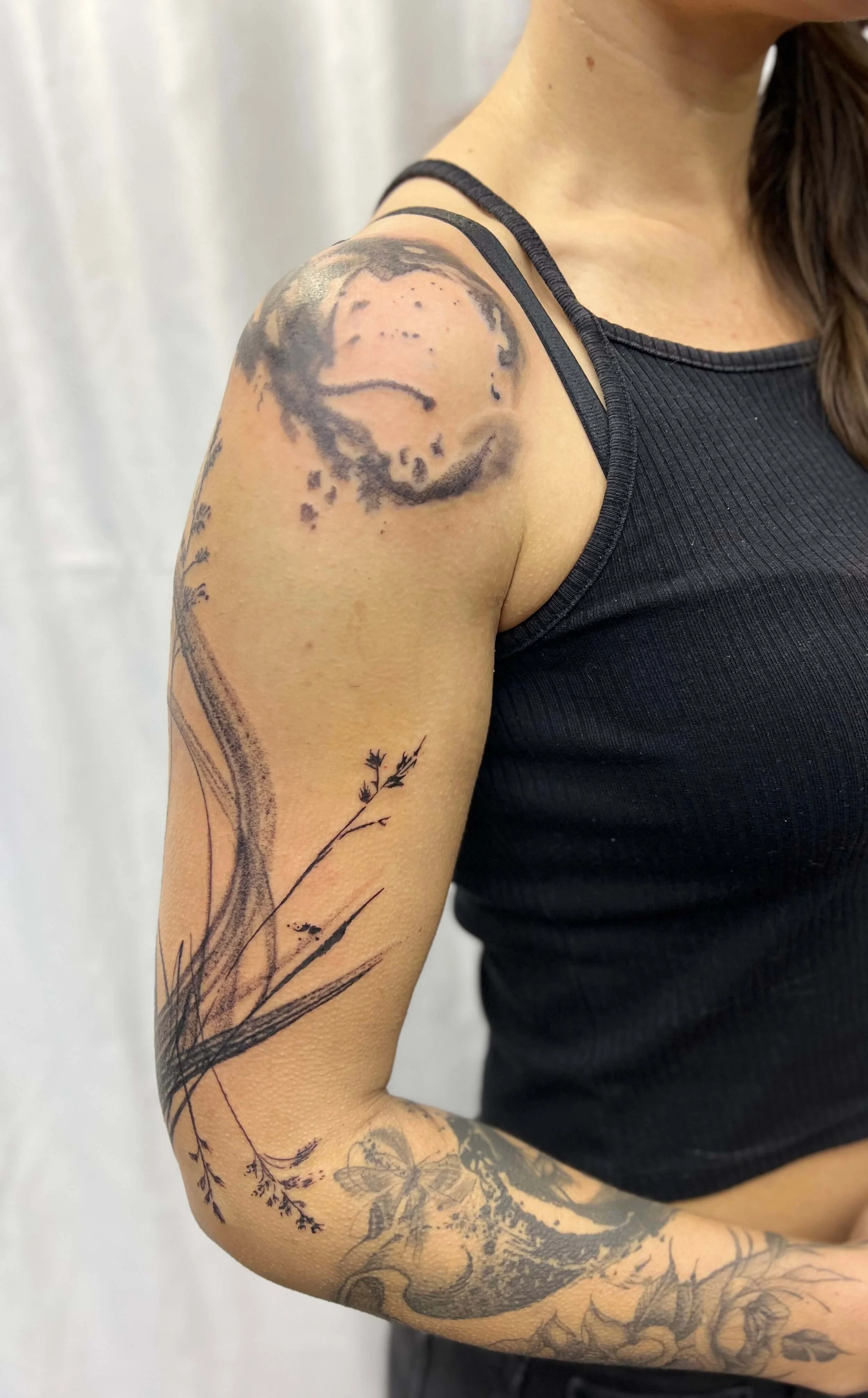 Blackwork shoulder composition featuring a stylised moon and flowing botanical elements.