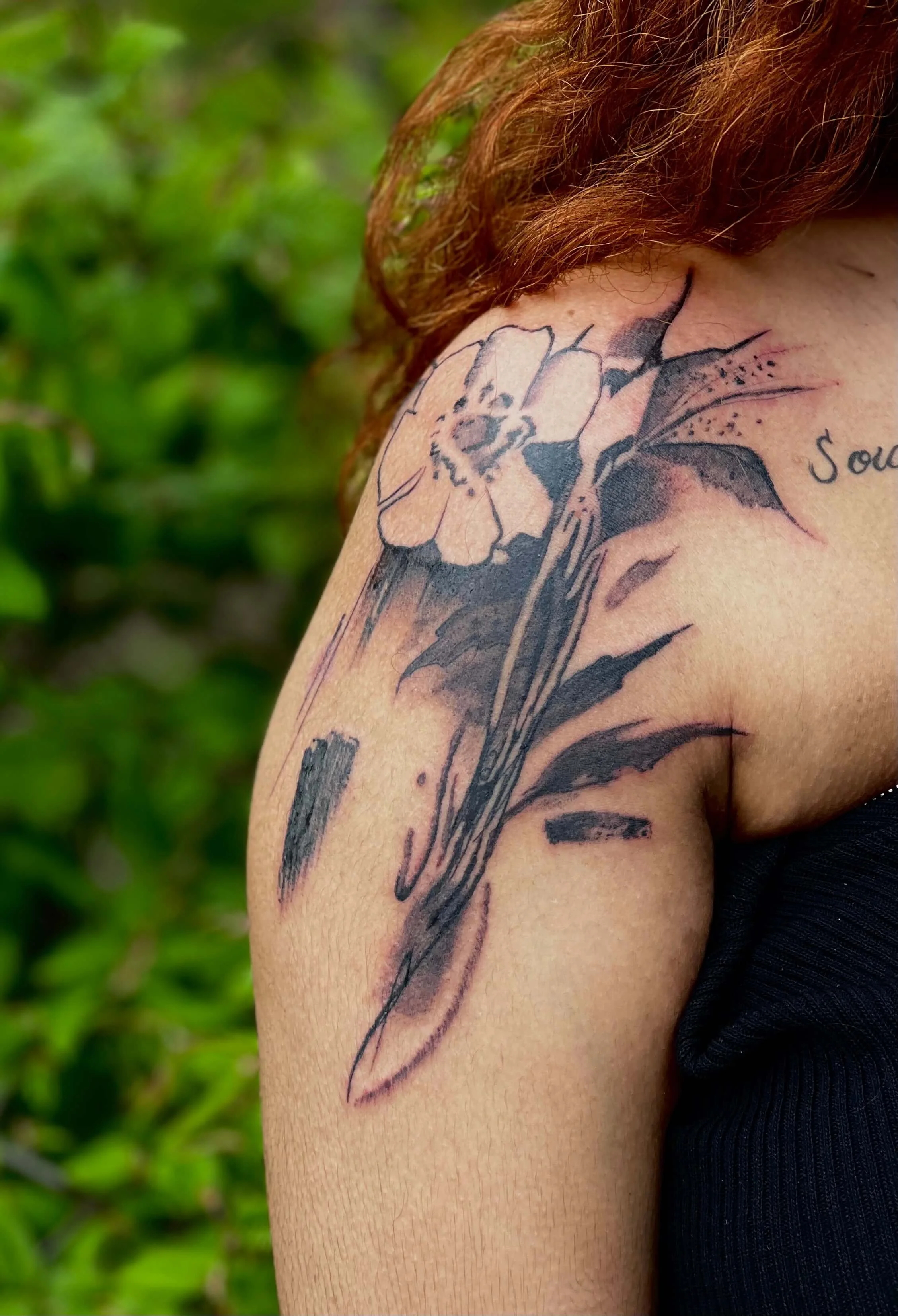 Abstract black ink floral tattoo on the arm featuring a bee motif with organic linework.