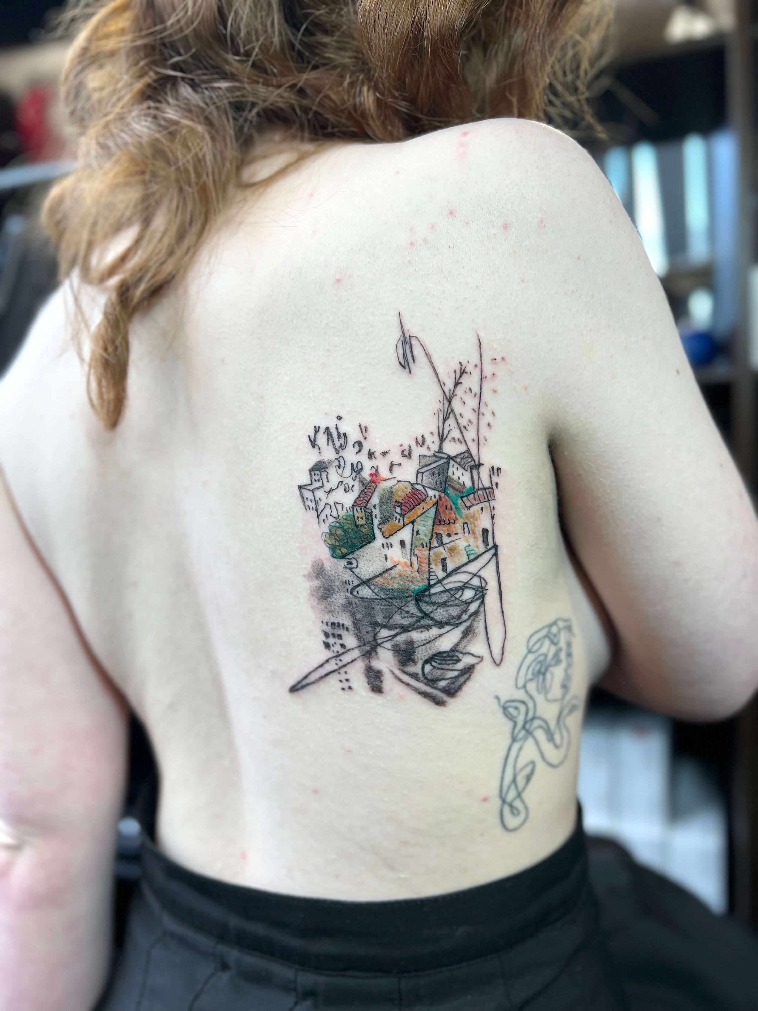 Colour abstract tattoo of a cityscape and trees placed on the upper back near the shoulder.