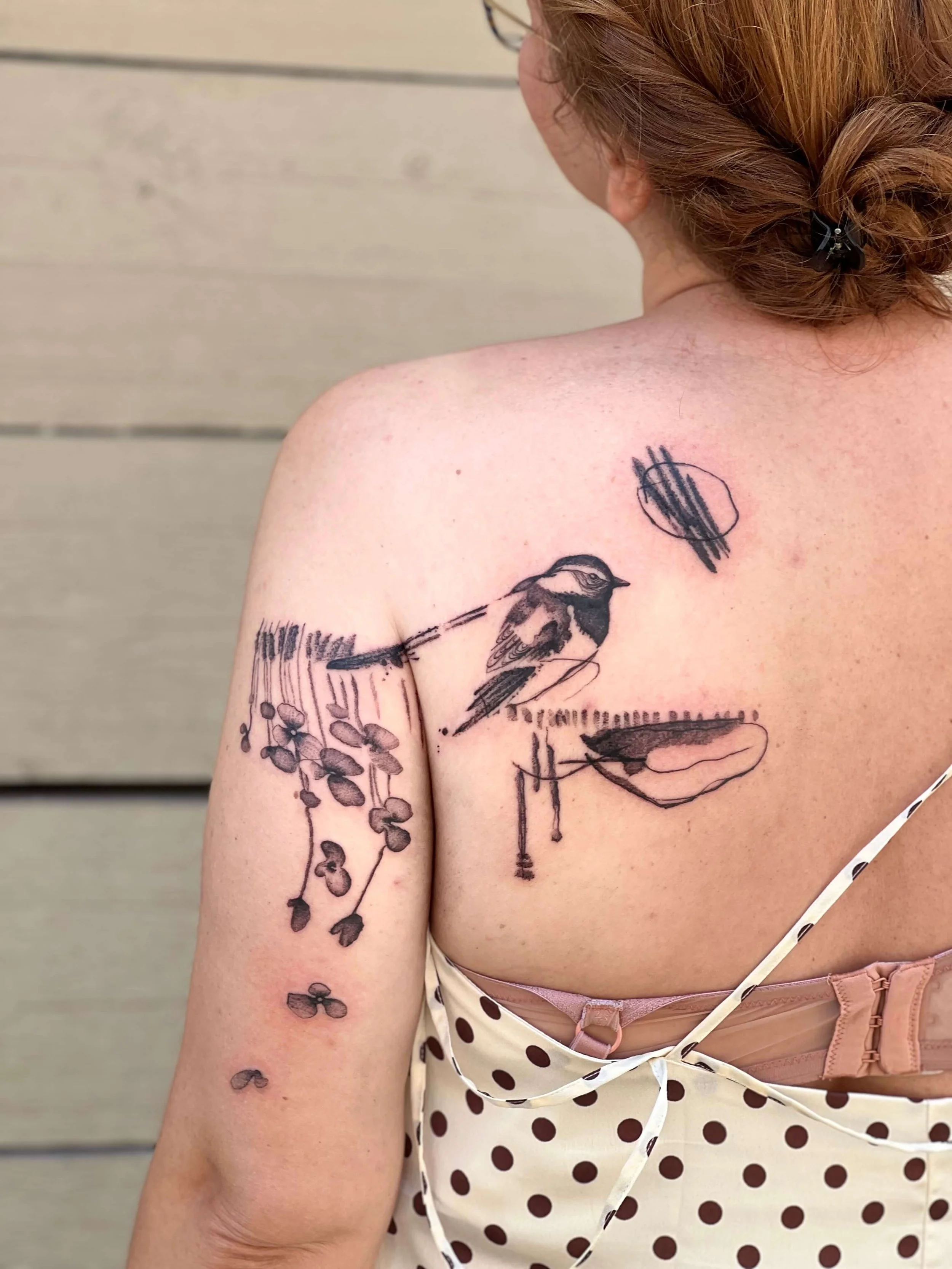 Abstract black ink shoulder tattoo combining avian forms and graphic line elements in a minimalist composition.