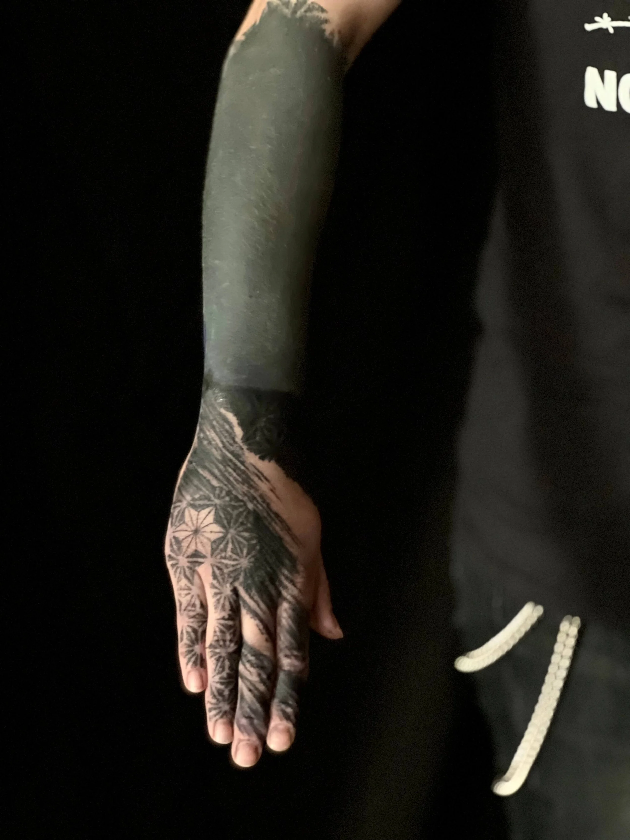Abstract blackwork tattoo sleeve extending from the forearm to the hand with dense dark composition.