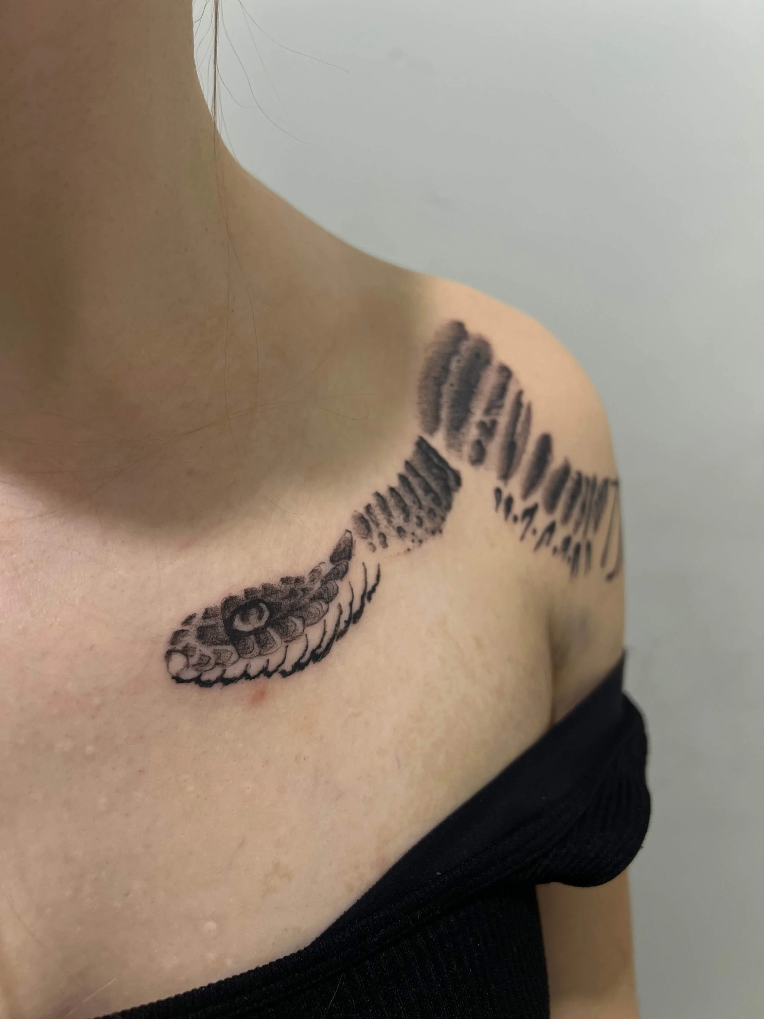 Tattoo of a snake coiled around the shoulder on a person's upper chest.