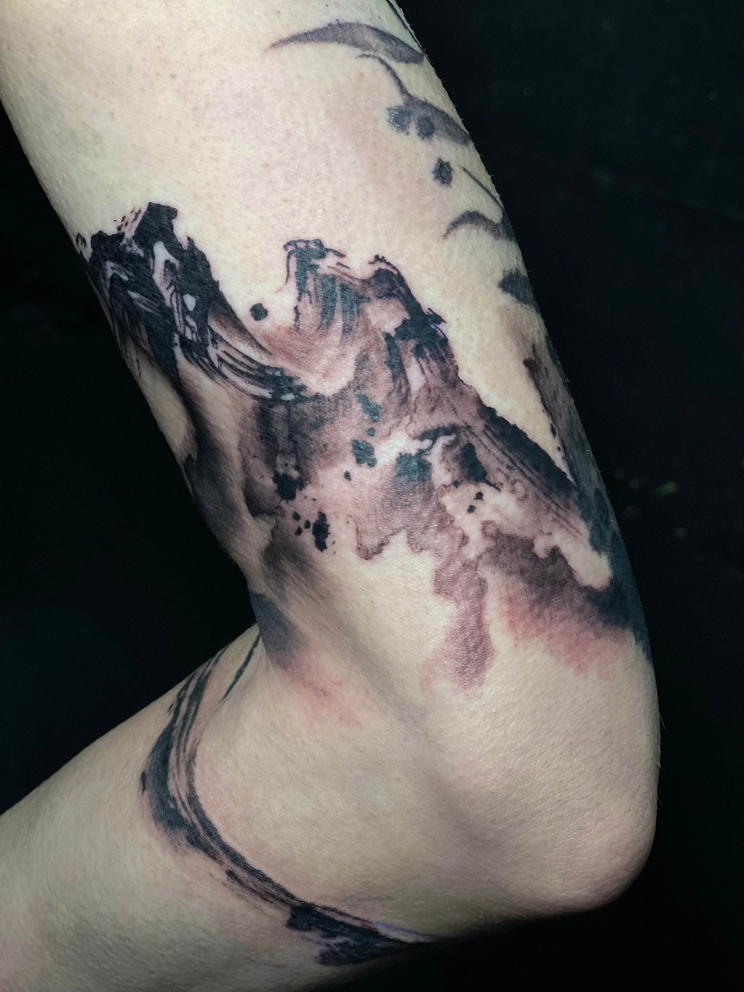 Abstract black and grey landscape tattoo featuring stylised mountains and cloud forms in expressive ink style.