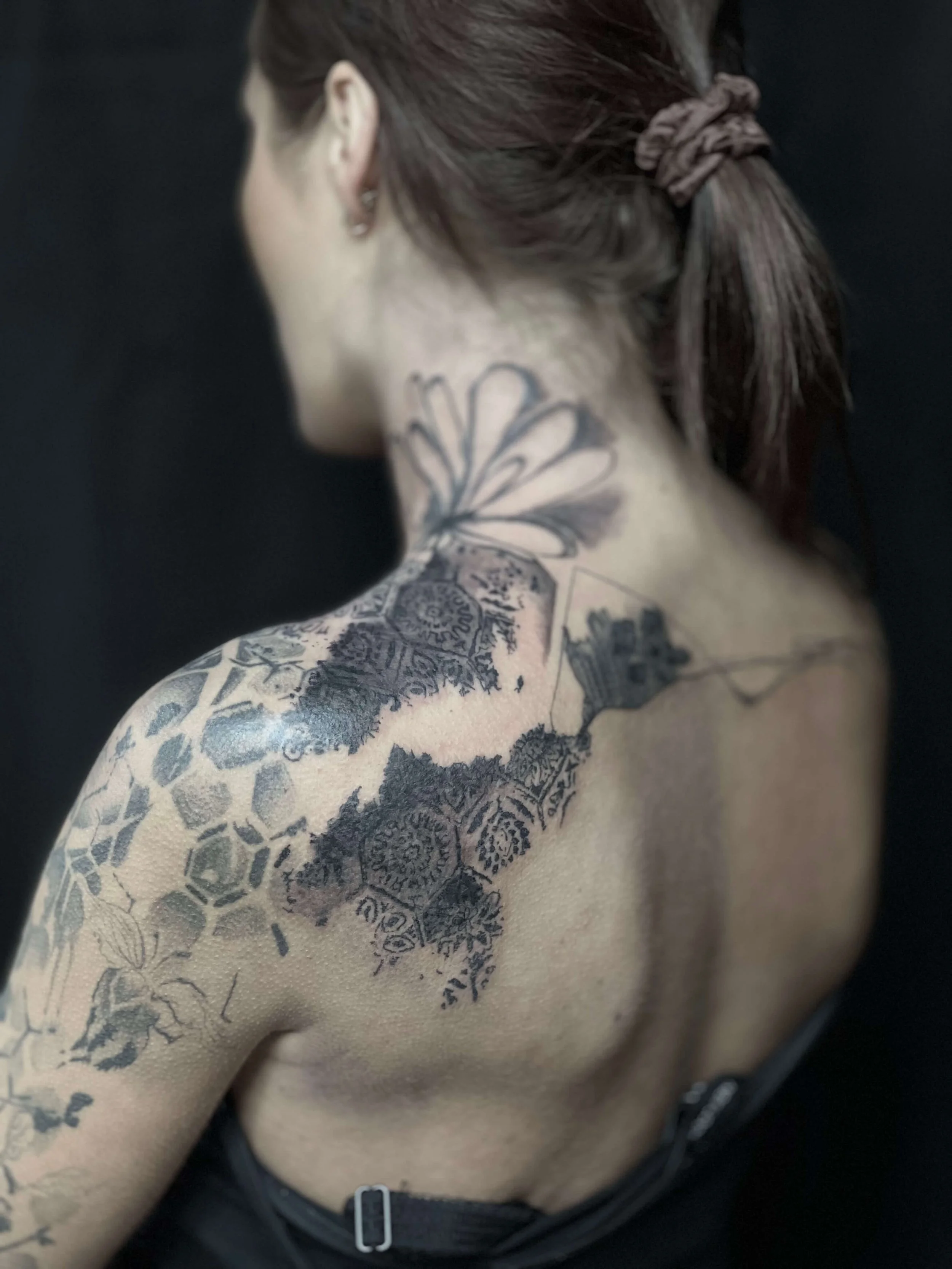 Large abstract blackwork tattoo across the shoulder and neck with flowing organic composition.