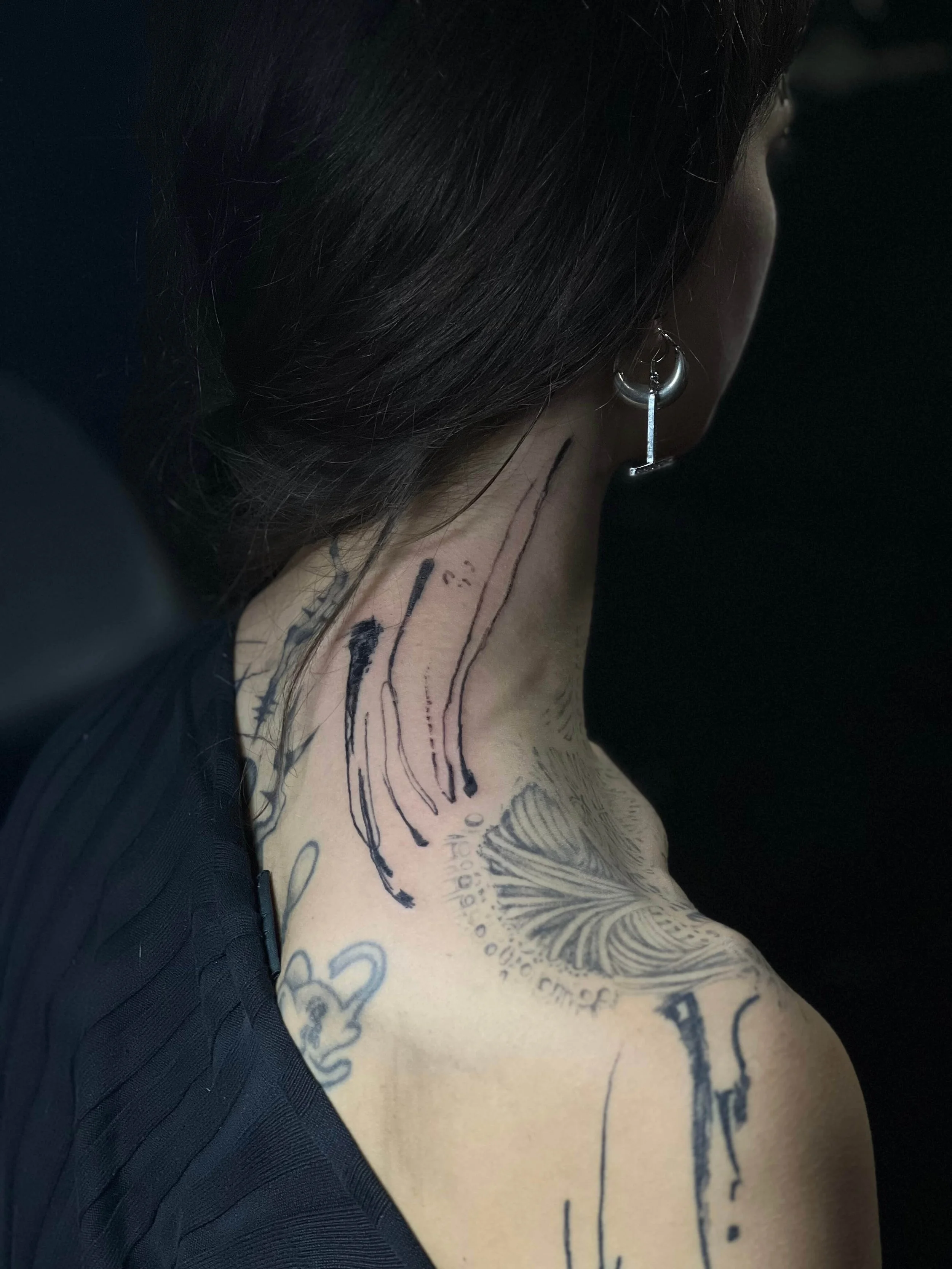 Contemporary abstract neck and shoulder tattoo in black ink with refined graphic detailing.