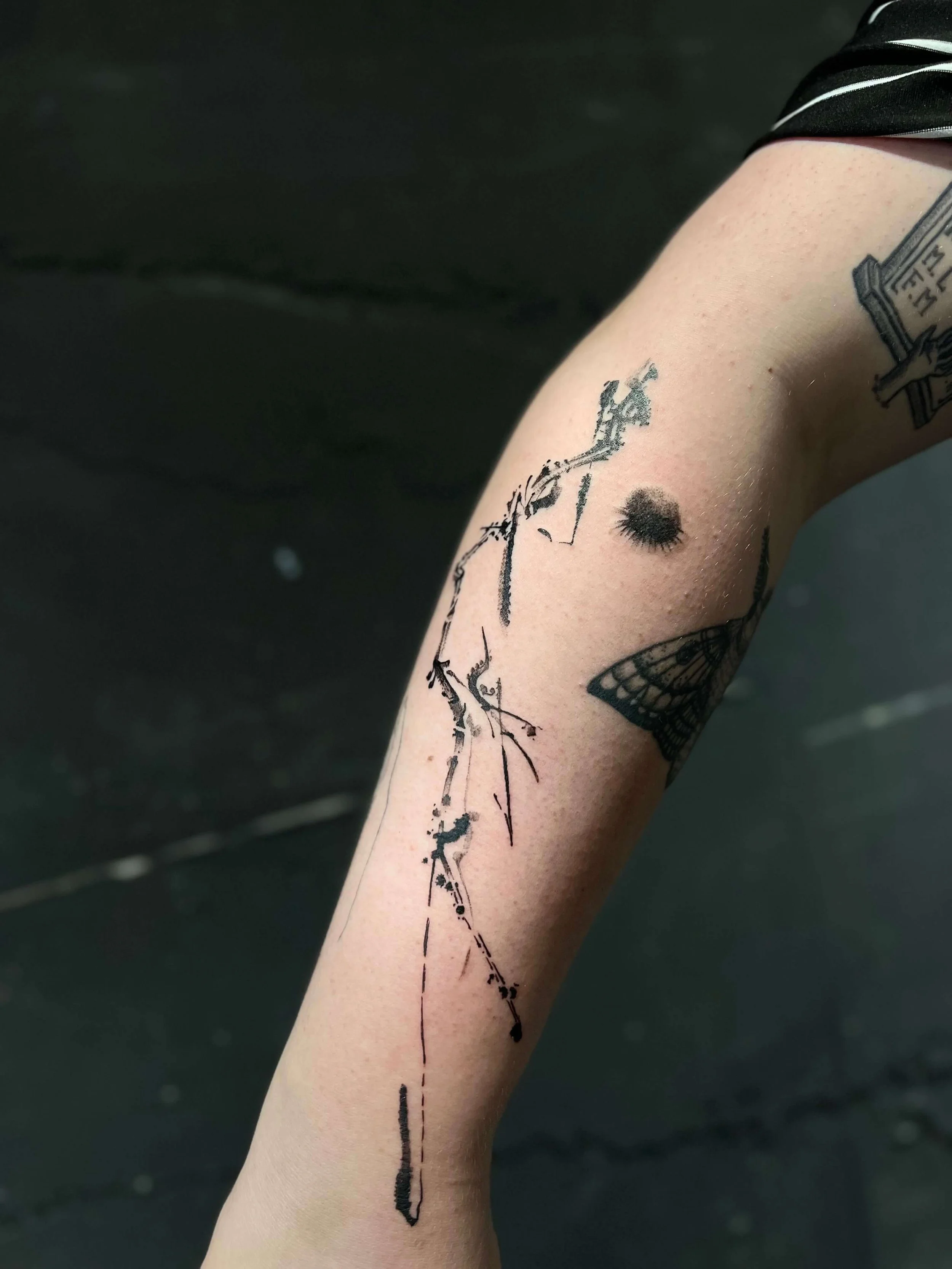 Contemporary abstract tattoo on the forearm combining figurative elements with clean black linework.