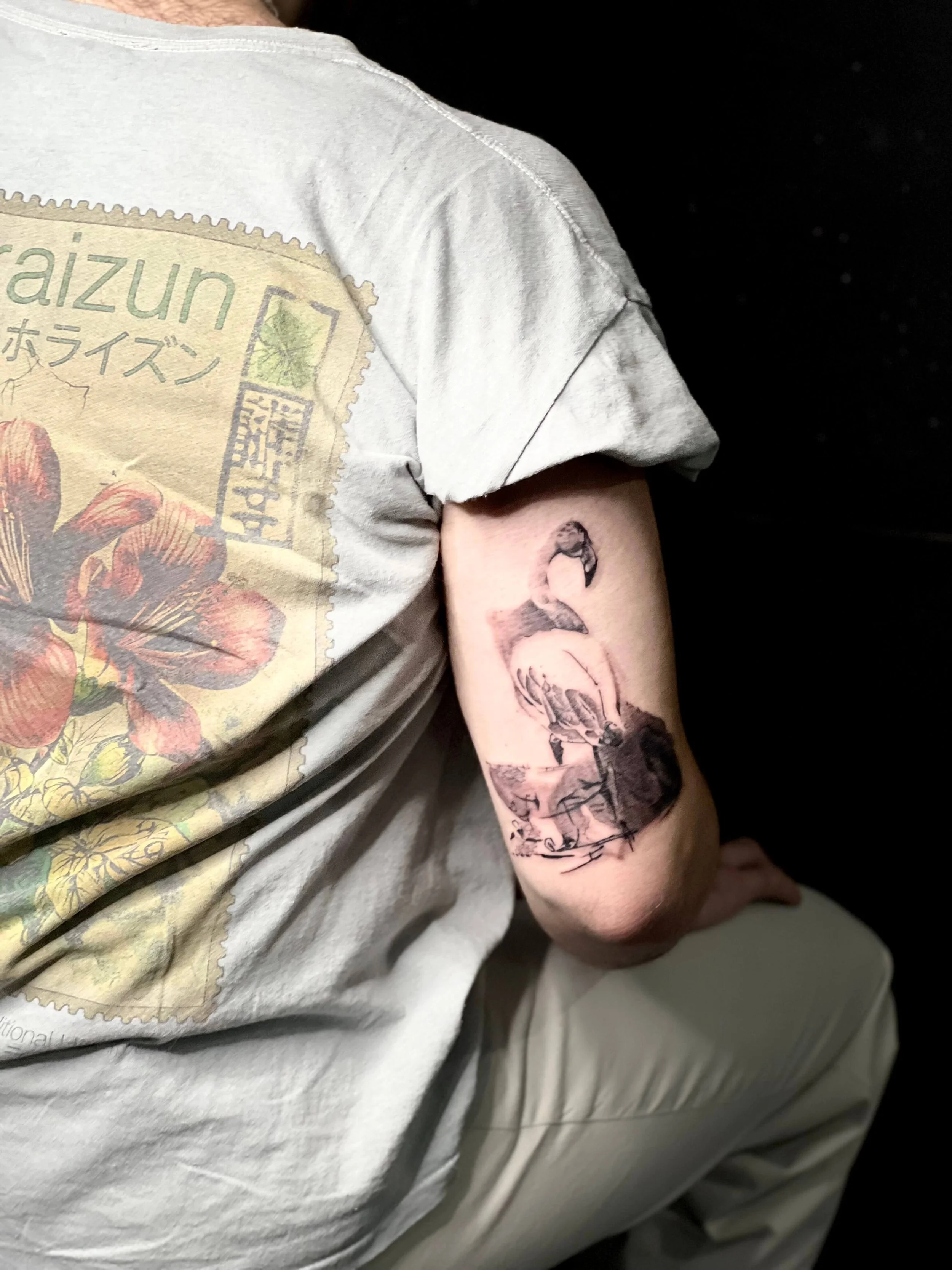 Abstract black ink upper arm tattoo featuring a stylised flamingo with graphic line composition.