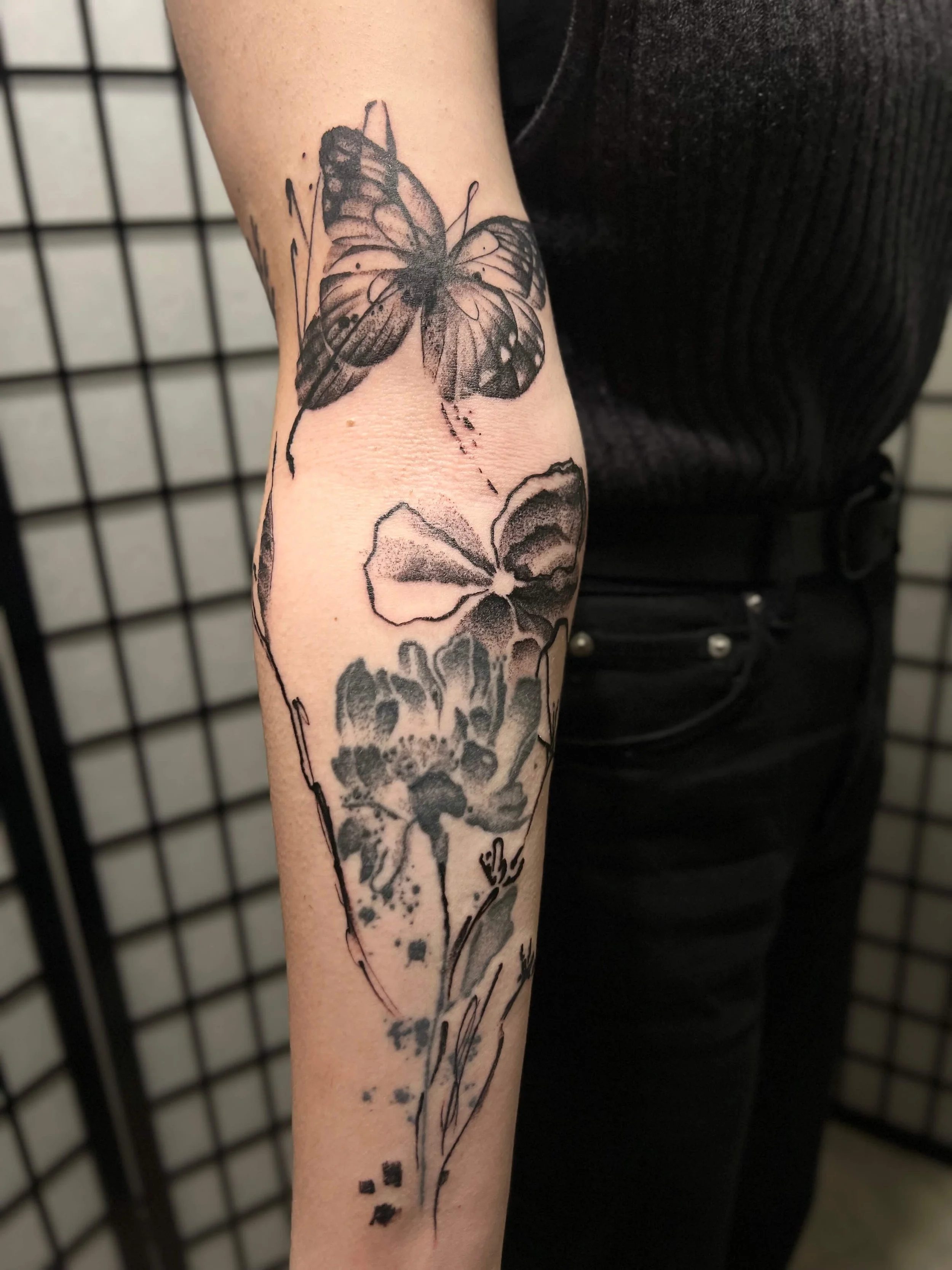 Abstract black and grey butterfly composition on the forearm with expressive ink splatter detailing.