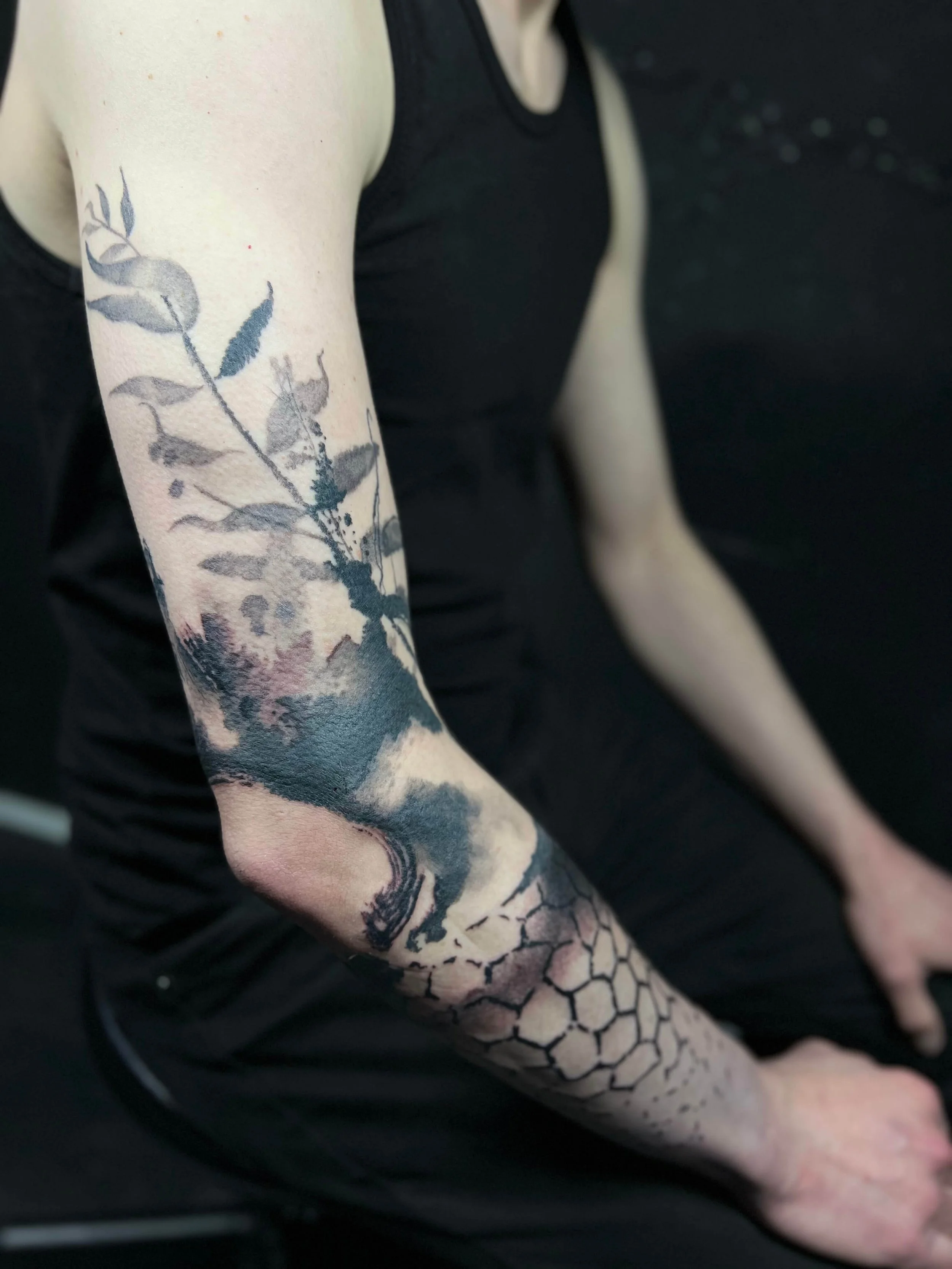 Blackwork sleeve composition combining botanical branch elements, mountain landscape detailing, and hexagon geometry.