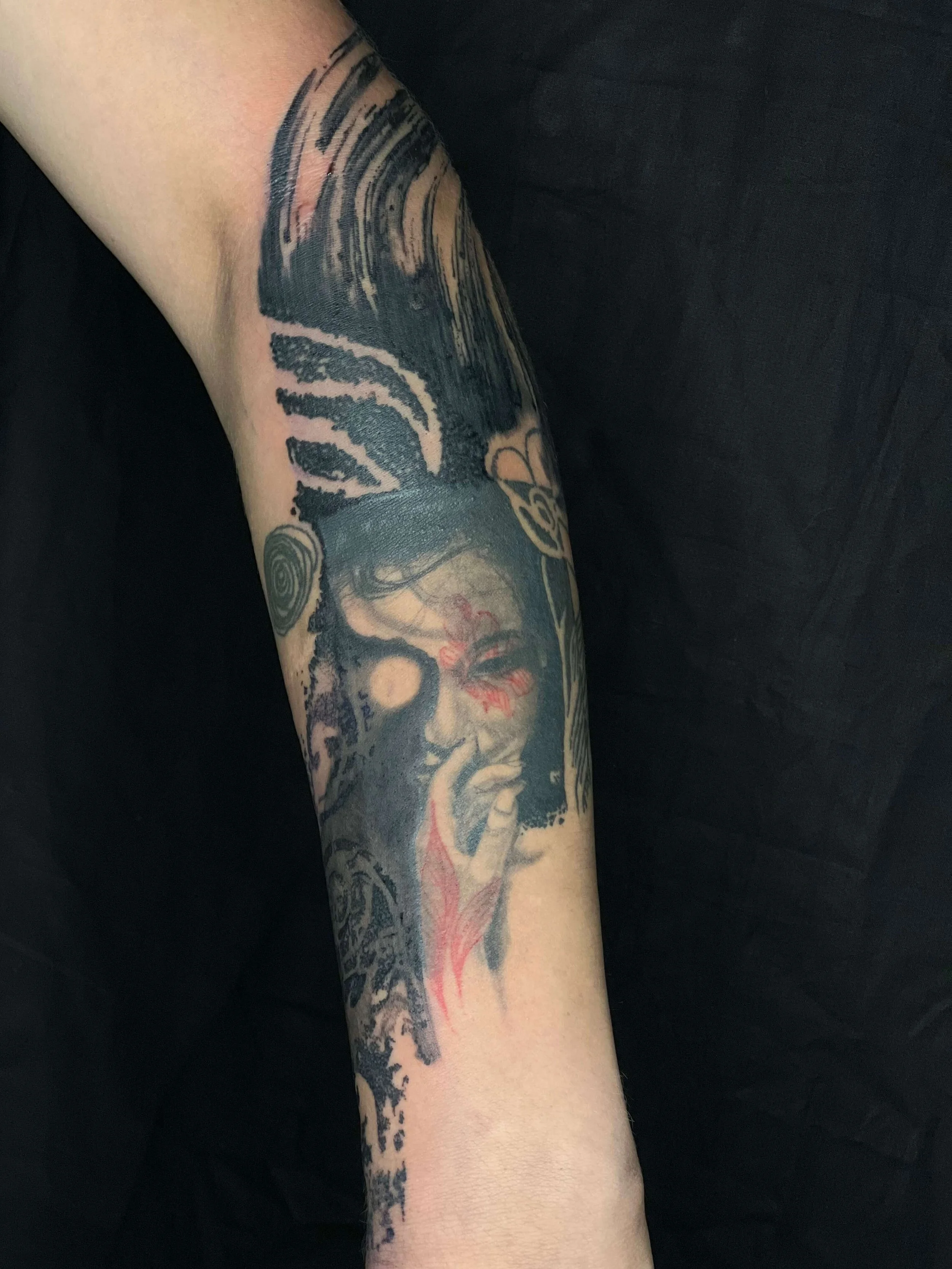 Abstract portrait tattoo of a woman with flowing hair and subtle red accents, created on the forearm by a London tattoo artist.