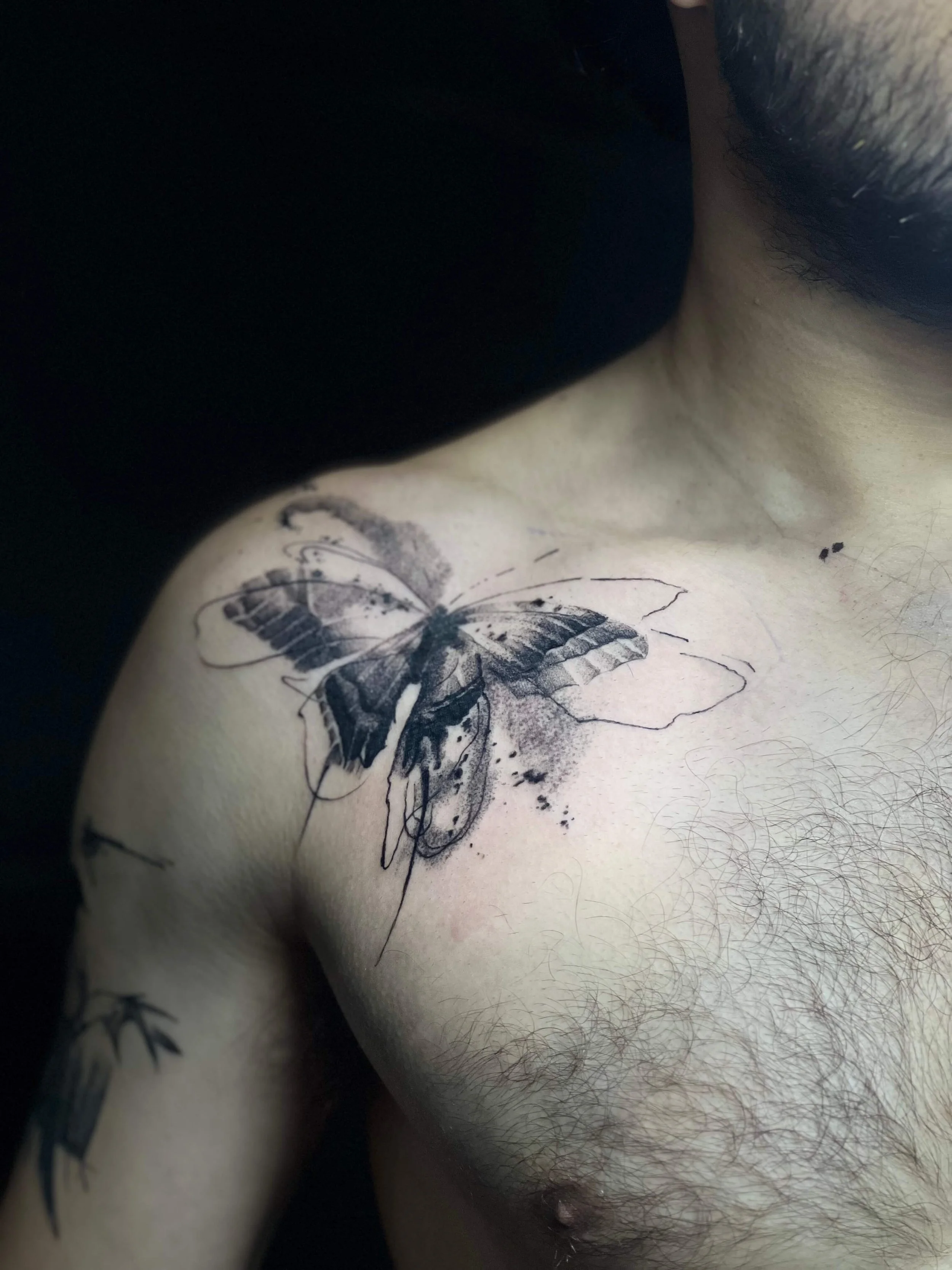 Minimal abstract butterfly composition on the shoulder in black and grey ink.
