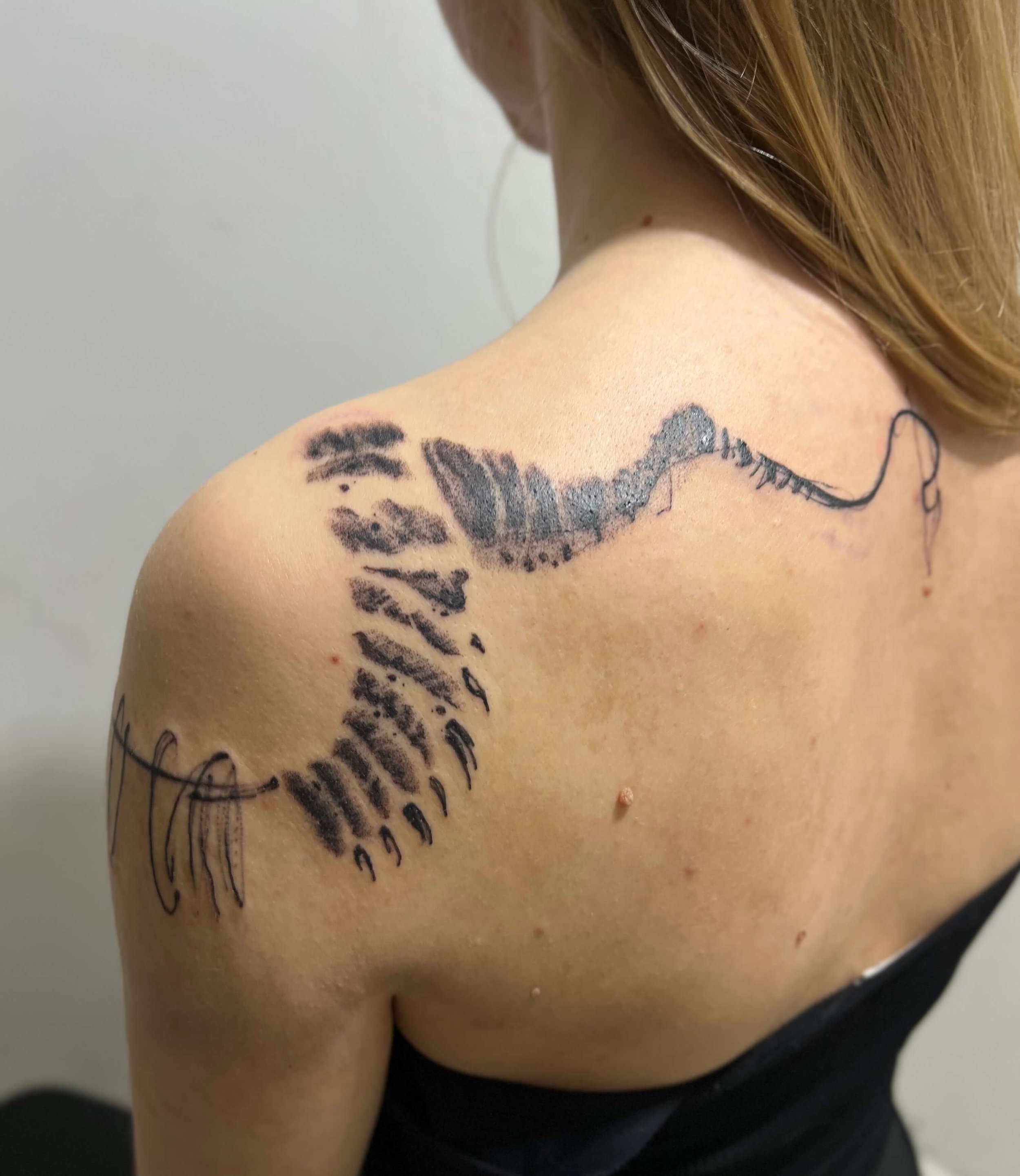 Abstract blackwork snake tattoo wrapping across the shoulder with fluid, organic line composition.