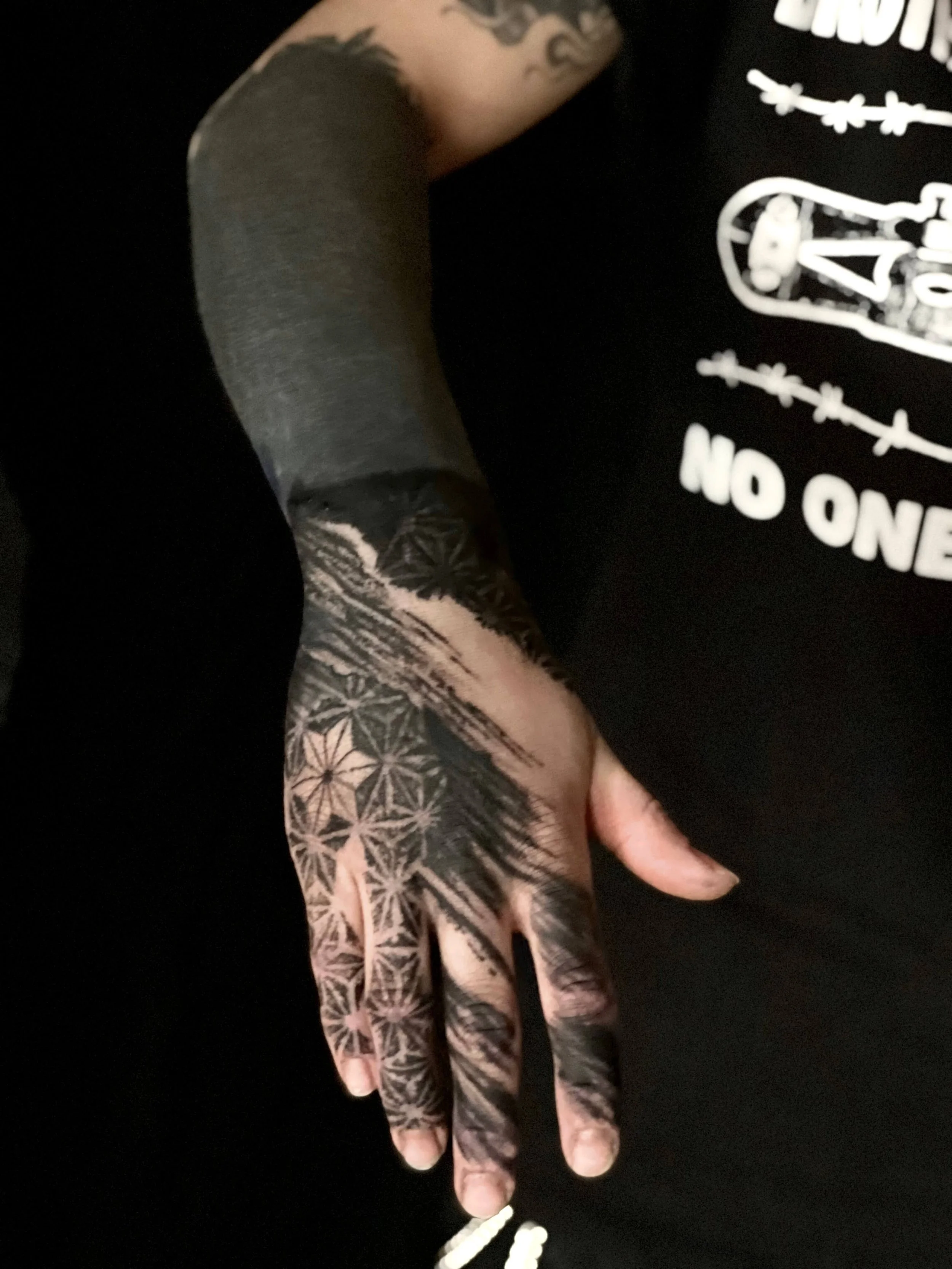 Abstract black ink tattoo covering the hand and forearm with bold graphic shapes and flowing linework.