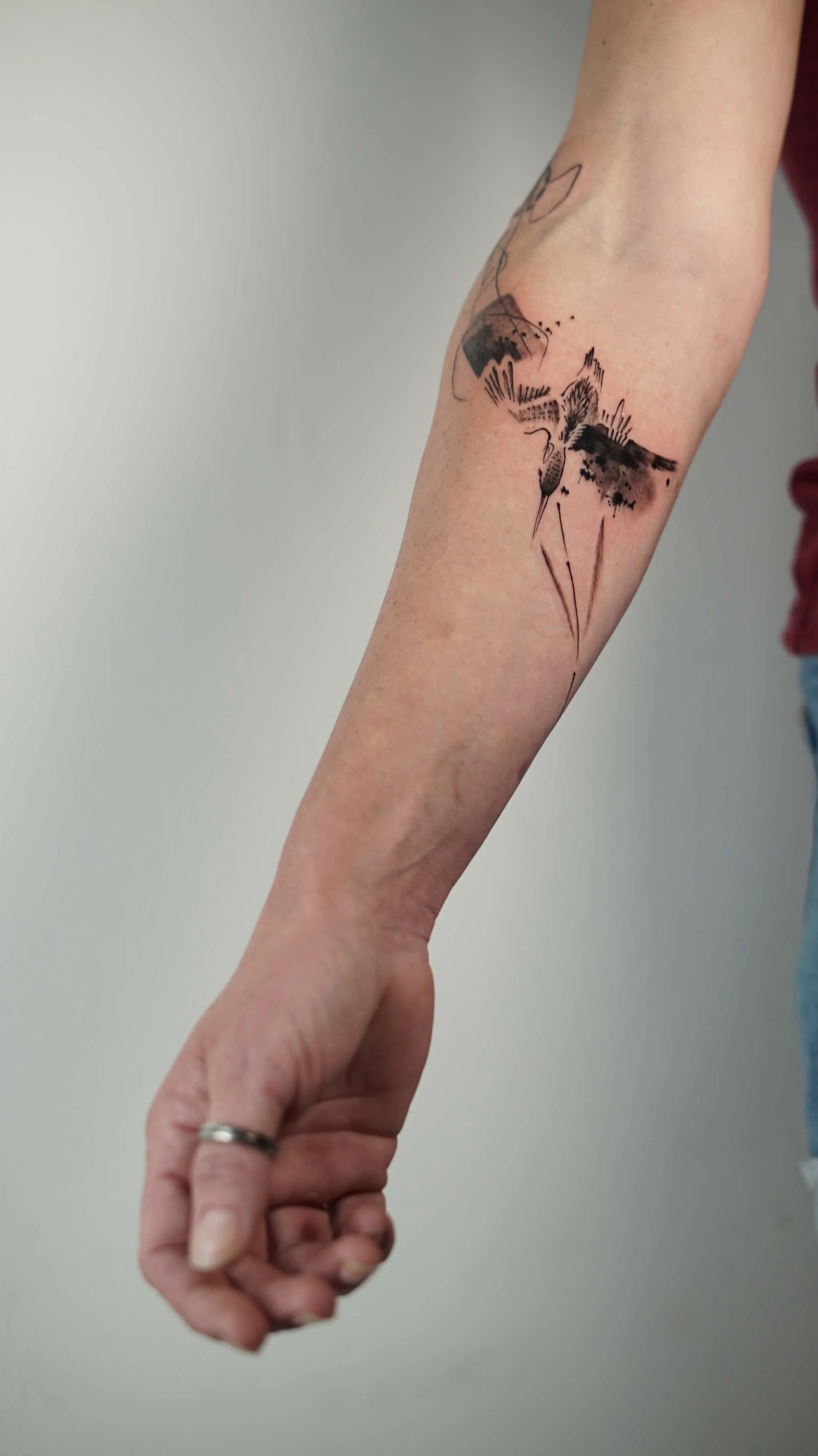 Abstract bird tattoo in black ink on the arm, combining minimal structure and expressive linework.