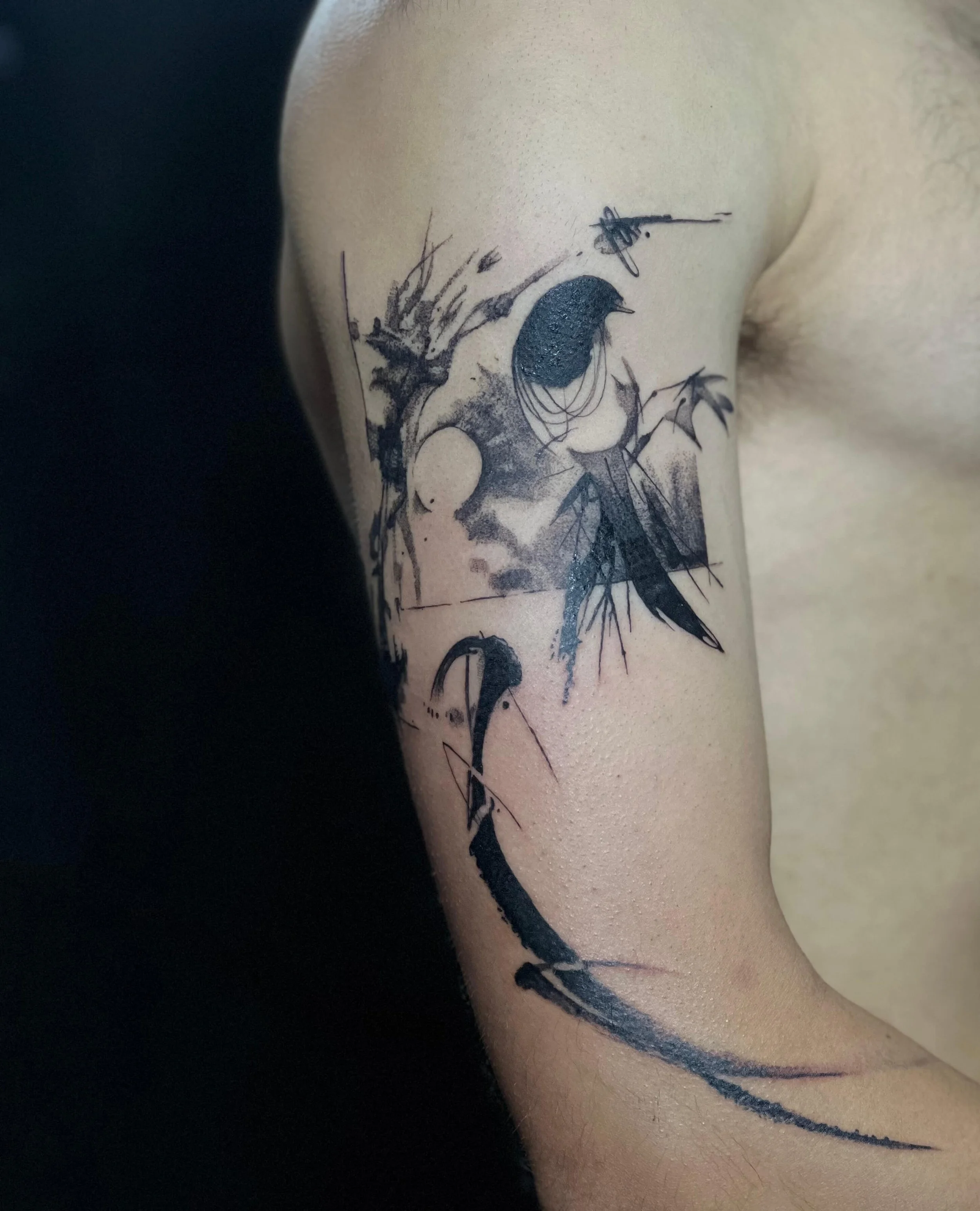 Contemporary abstract tattoo on the upper arm featuring symbolic bird and moon elements with fluid black linework.
