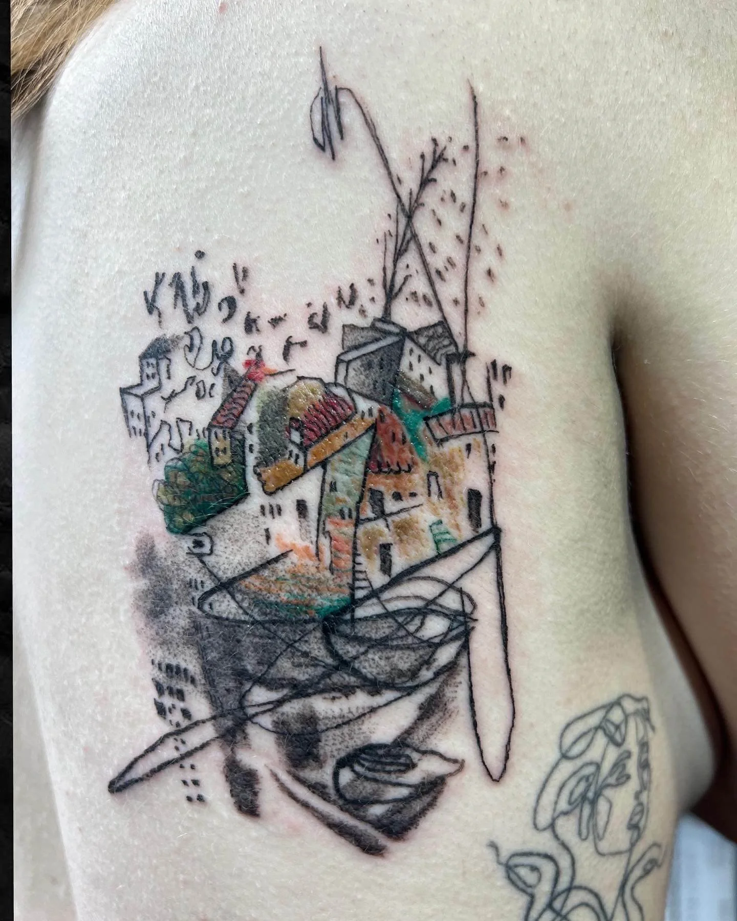 Detailed abstract cityscape tattoo combining colour and black linework on skin.