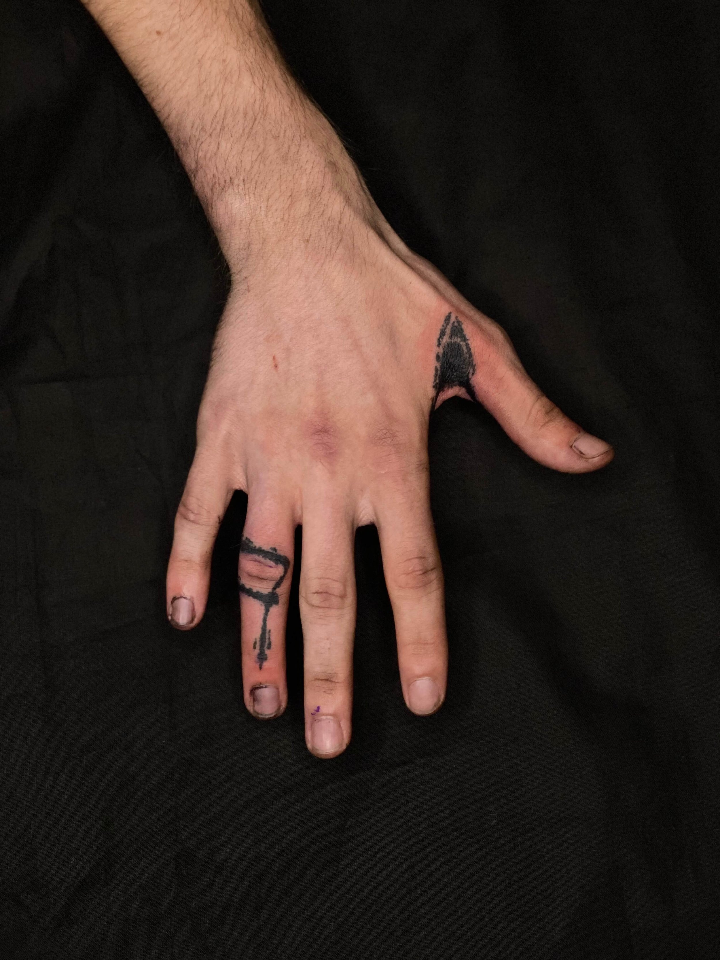 Abstract hand tattoo in black ink featuring graphic linework across the fingers and thumb.