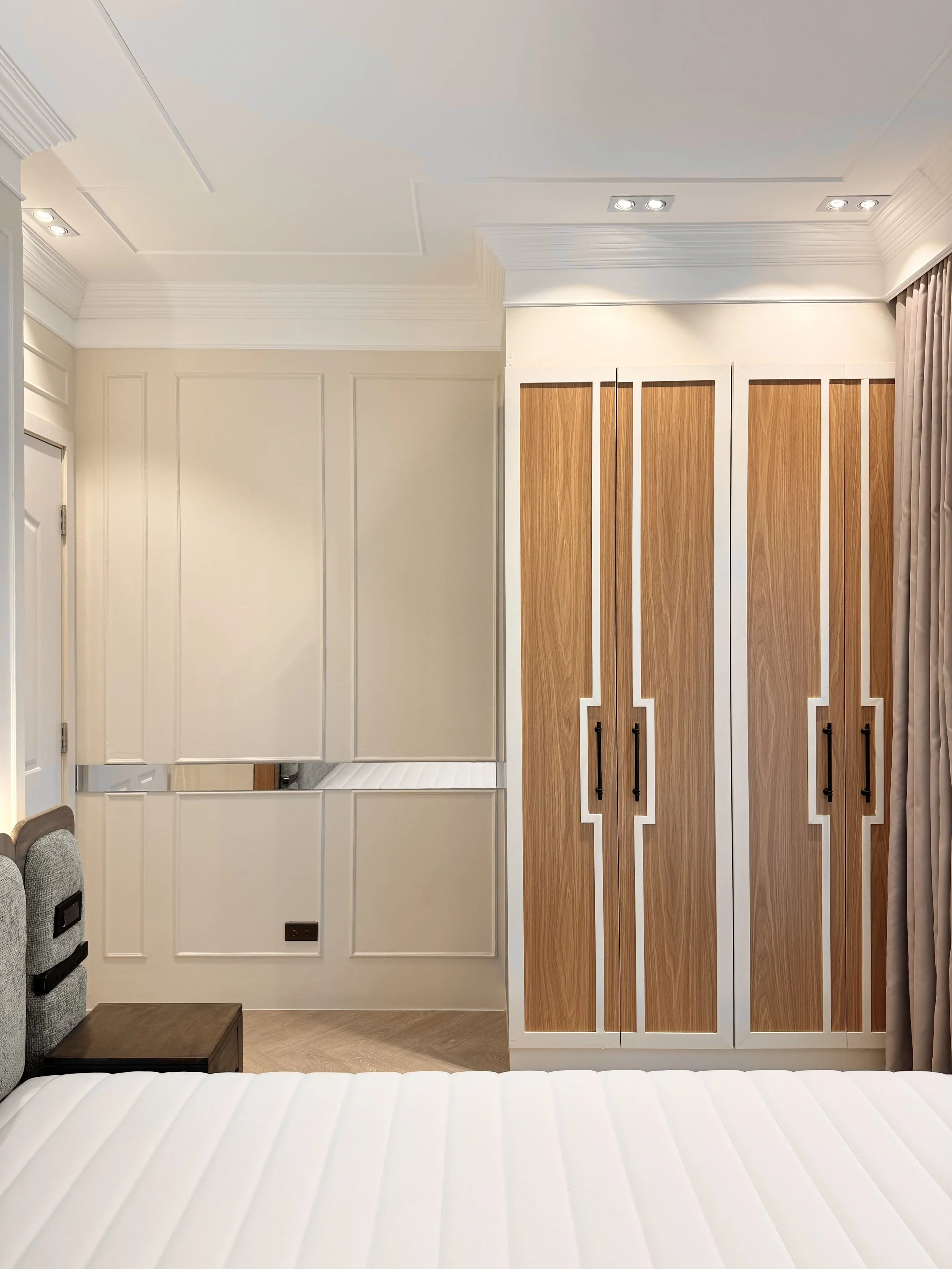 Interior of a bedroom with a white bed, a wooden wardrobe, and wall paneling.