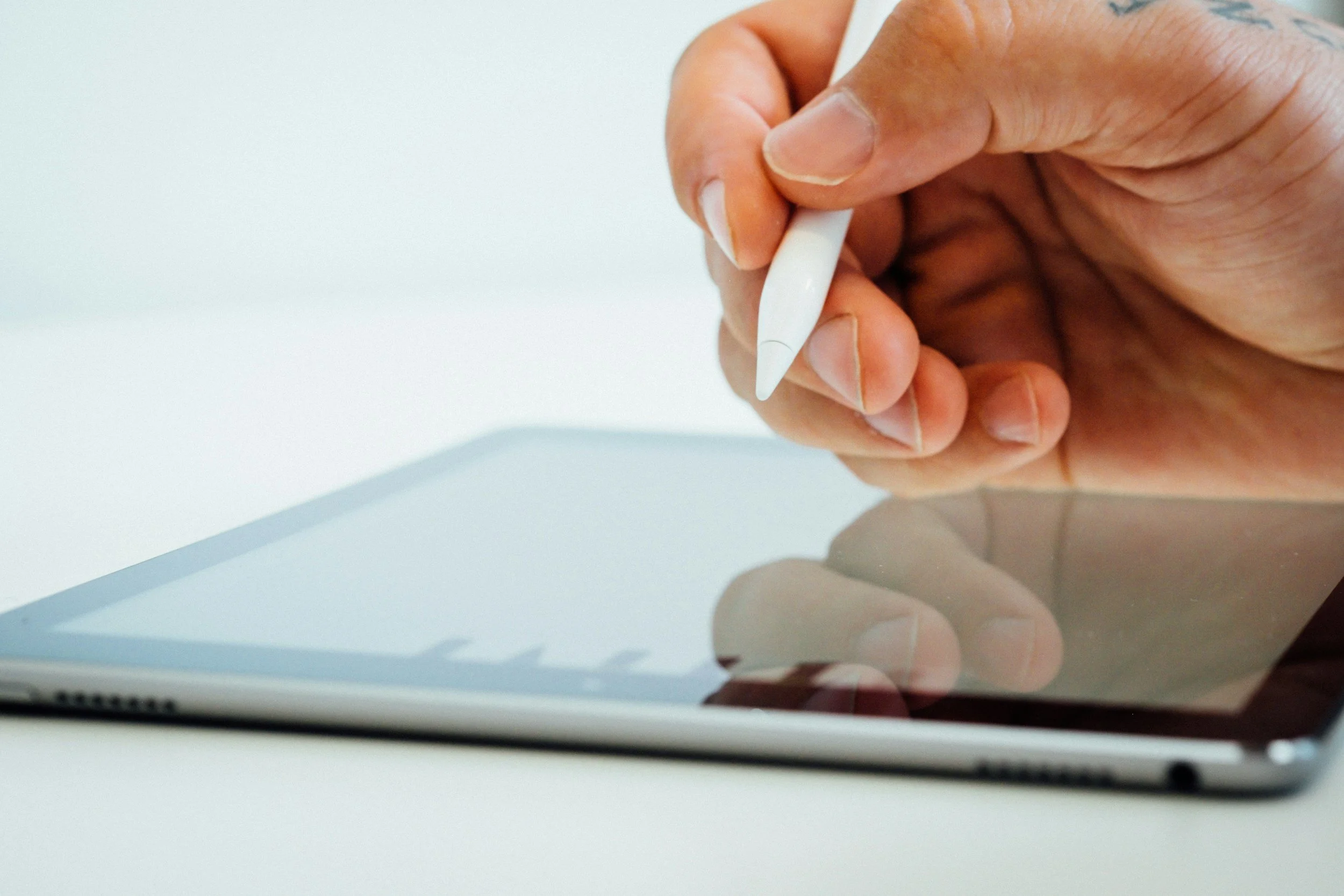 Close-up of person's hand holding a stylus pen over a tablet device on a white surface.